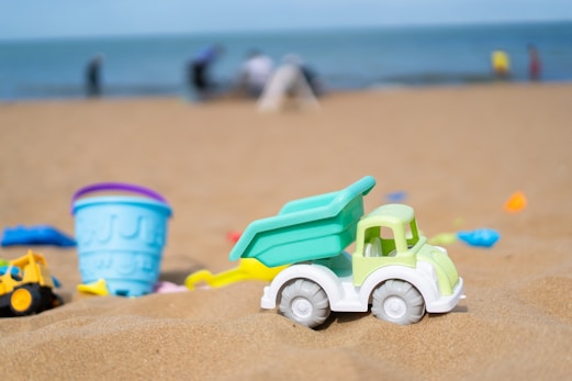 Toy trucks and buckets sit on a sandy beach.