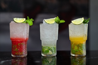 Three refreshing cocktails, garnished with limes and mint.
