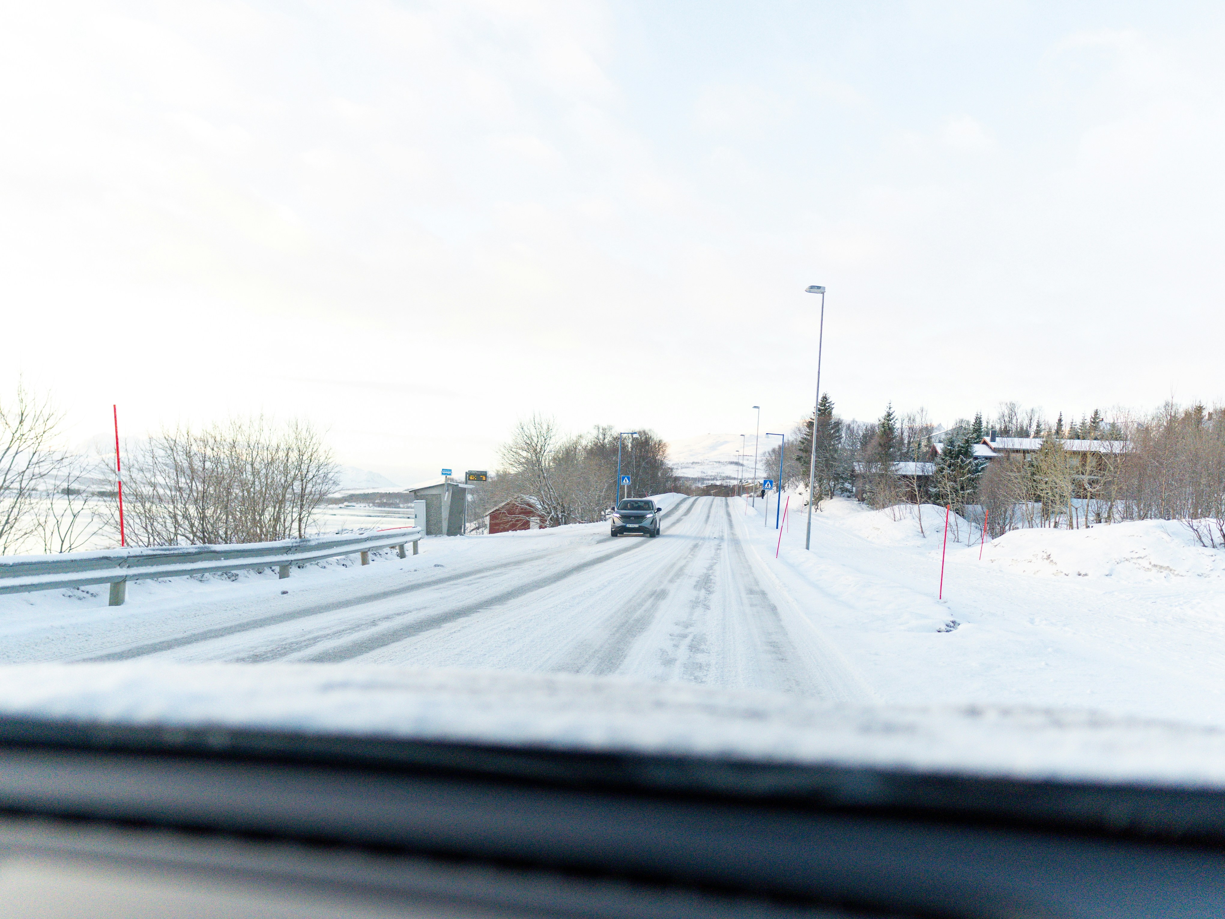 A snowy road with a car driving ahead.