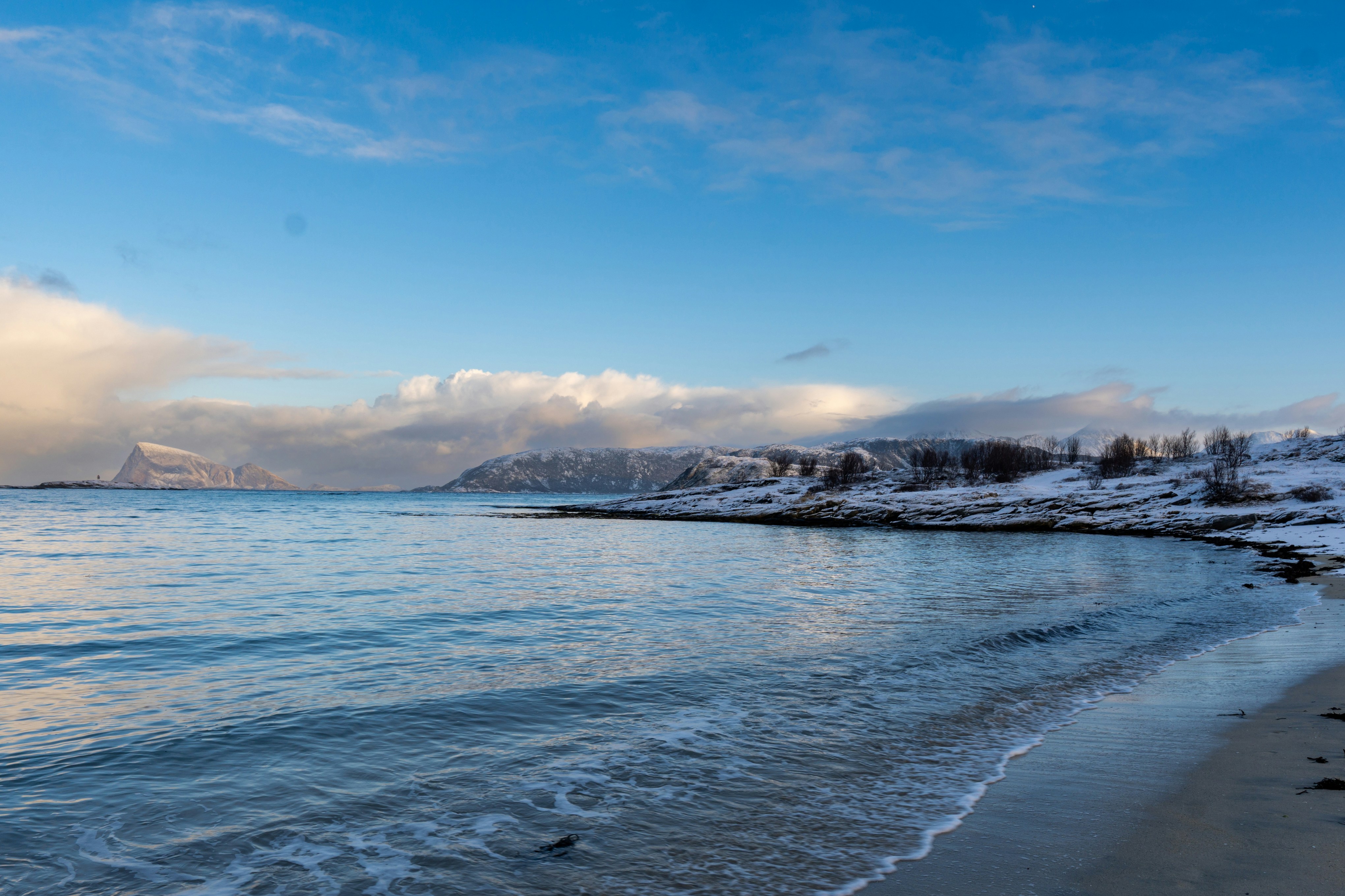 Wintery beach scene with snowy hills and blue sky.