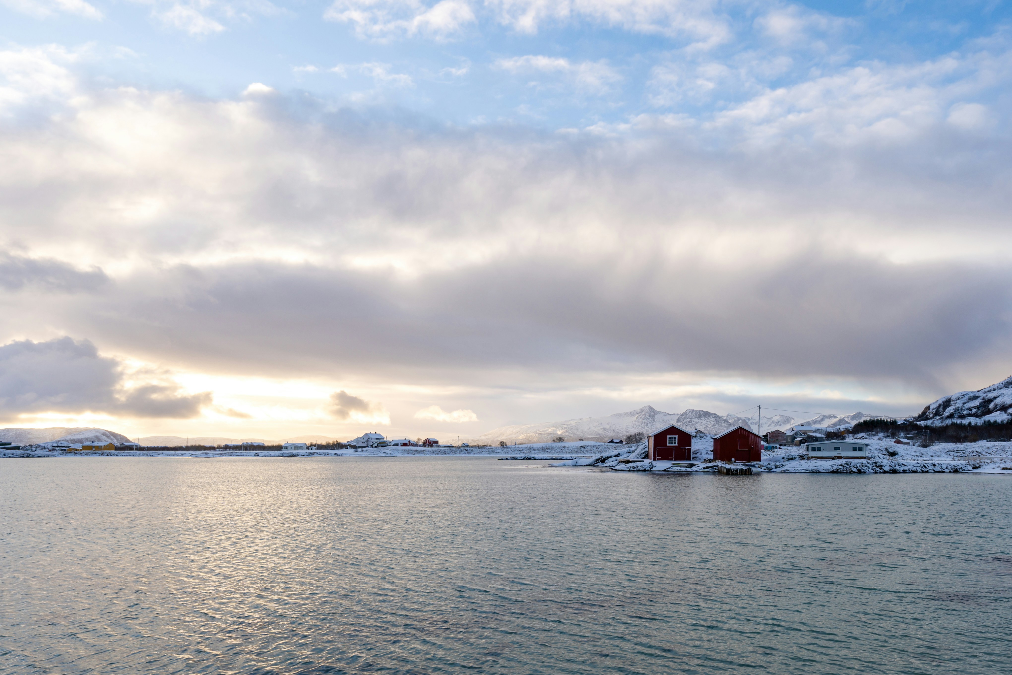 Red houses sit on a snowy shore by water.