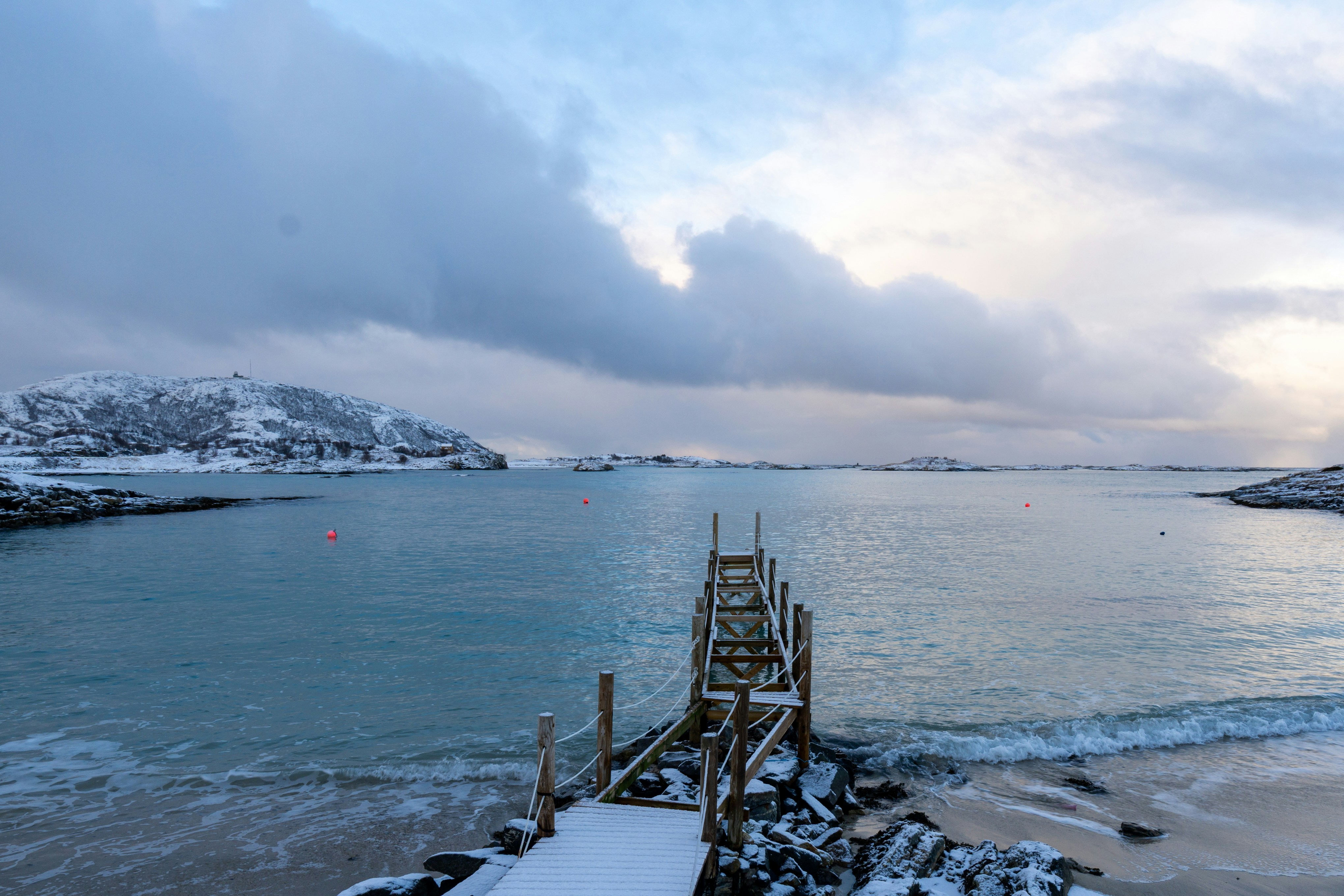 A wooden pier extends into a calm, snowy ocean.
