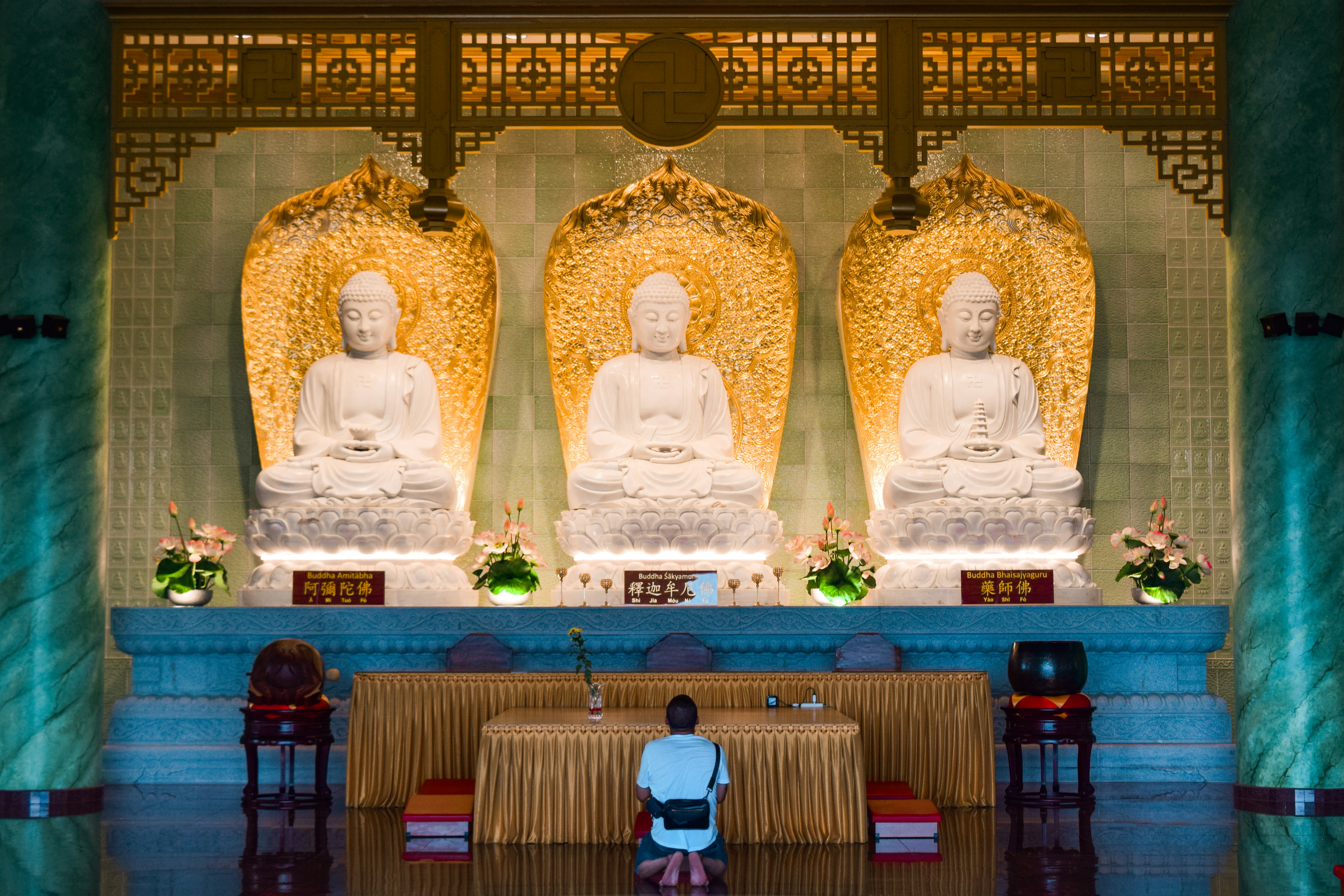 A person prays before three buddha statues.