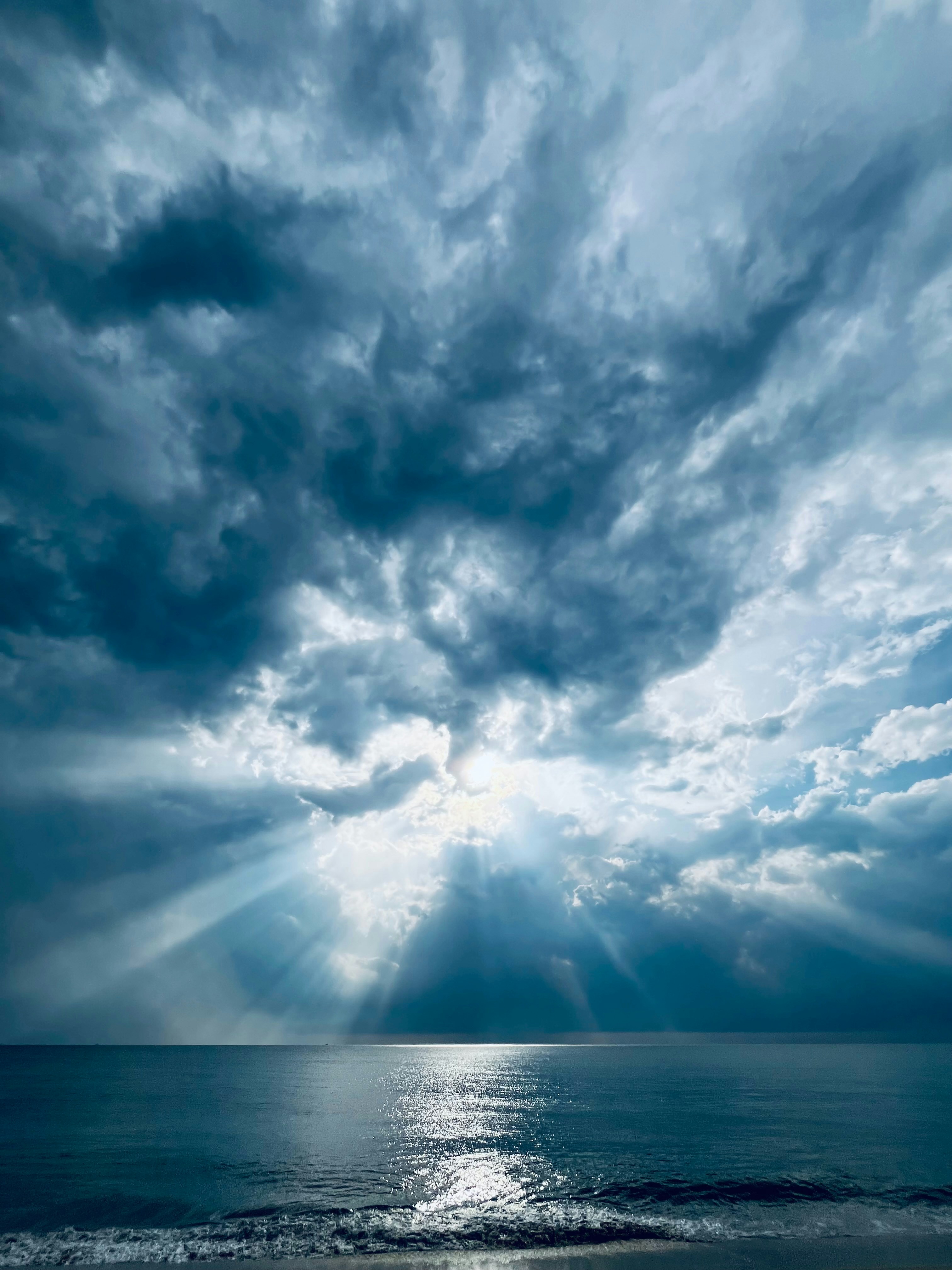 海の上の暗い曇り空から太陽の光が差し込んでいます。