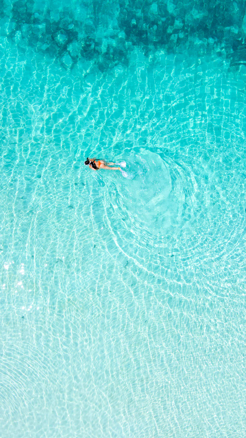 Person snorkeling in crystal-clear turquoise water over white sand