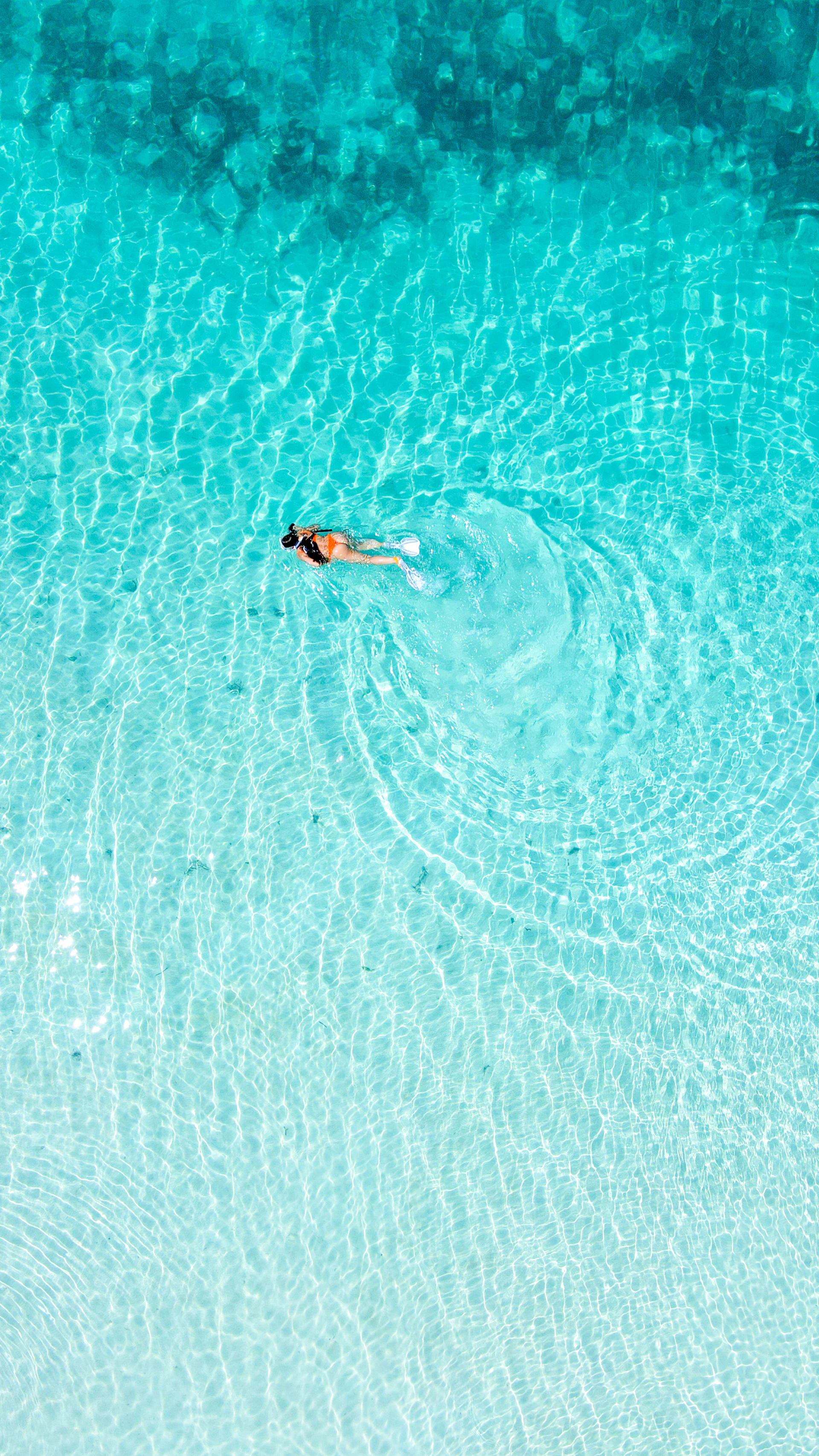 A person snorkels in crystal-clear turquoise water.