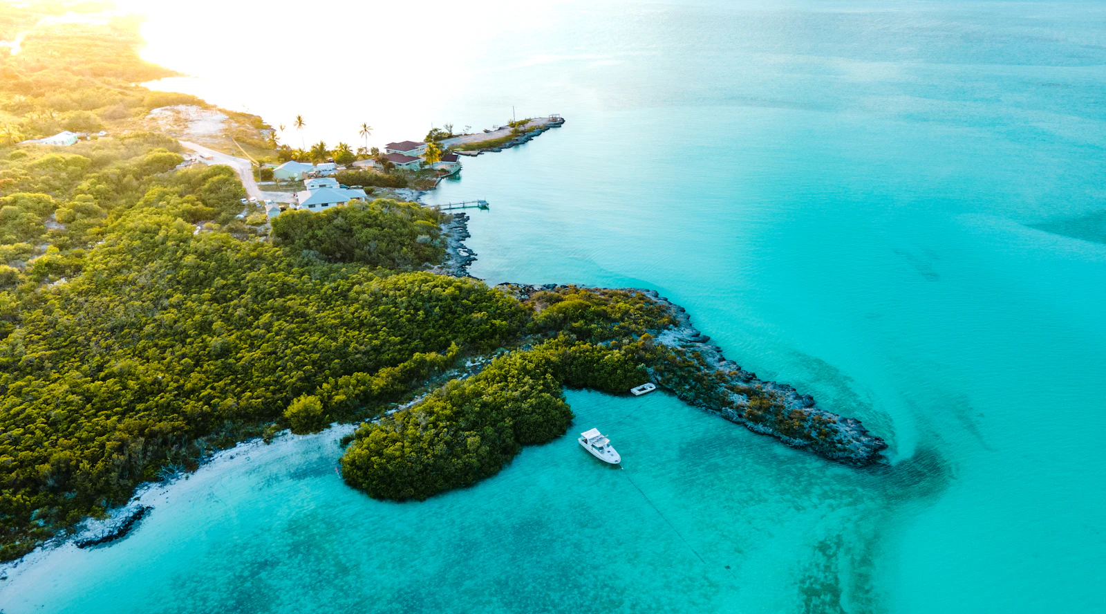 Aerial view of green cays and a boat anchored in the pale turquoise shallows of the Exumas