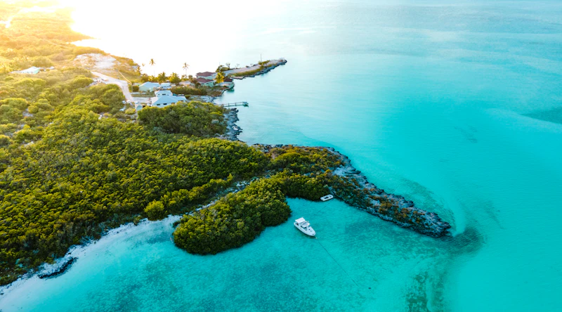 Aerial view of green cays and a boat anchored in the pale turquoise shallows of the Exumas
