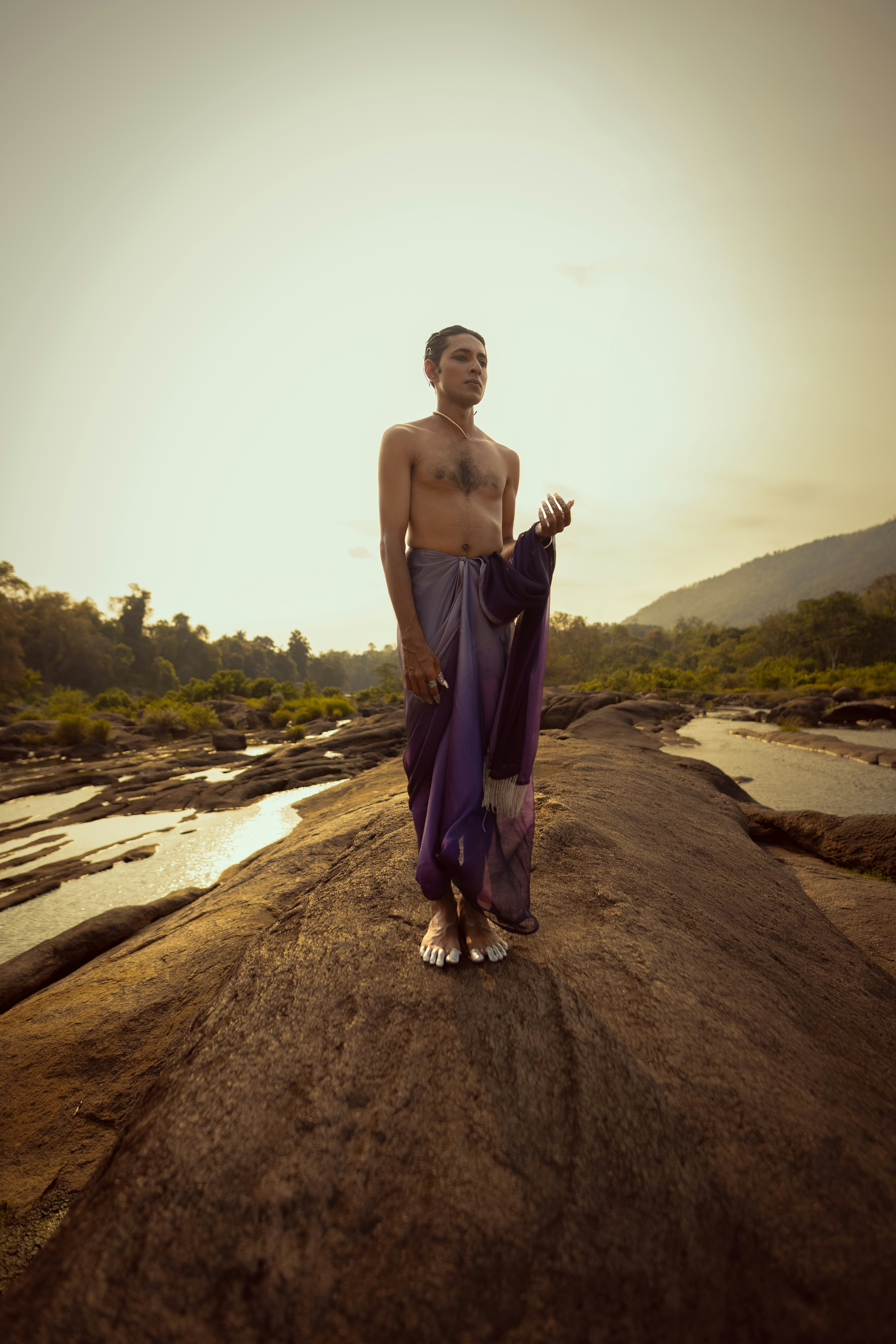 A man stands barefoot on a rocky outcrop.