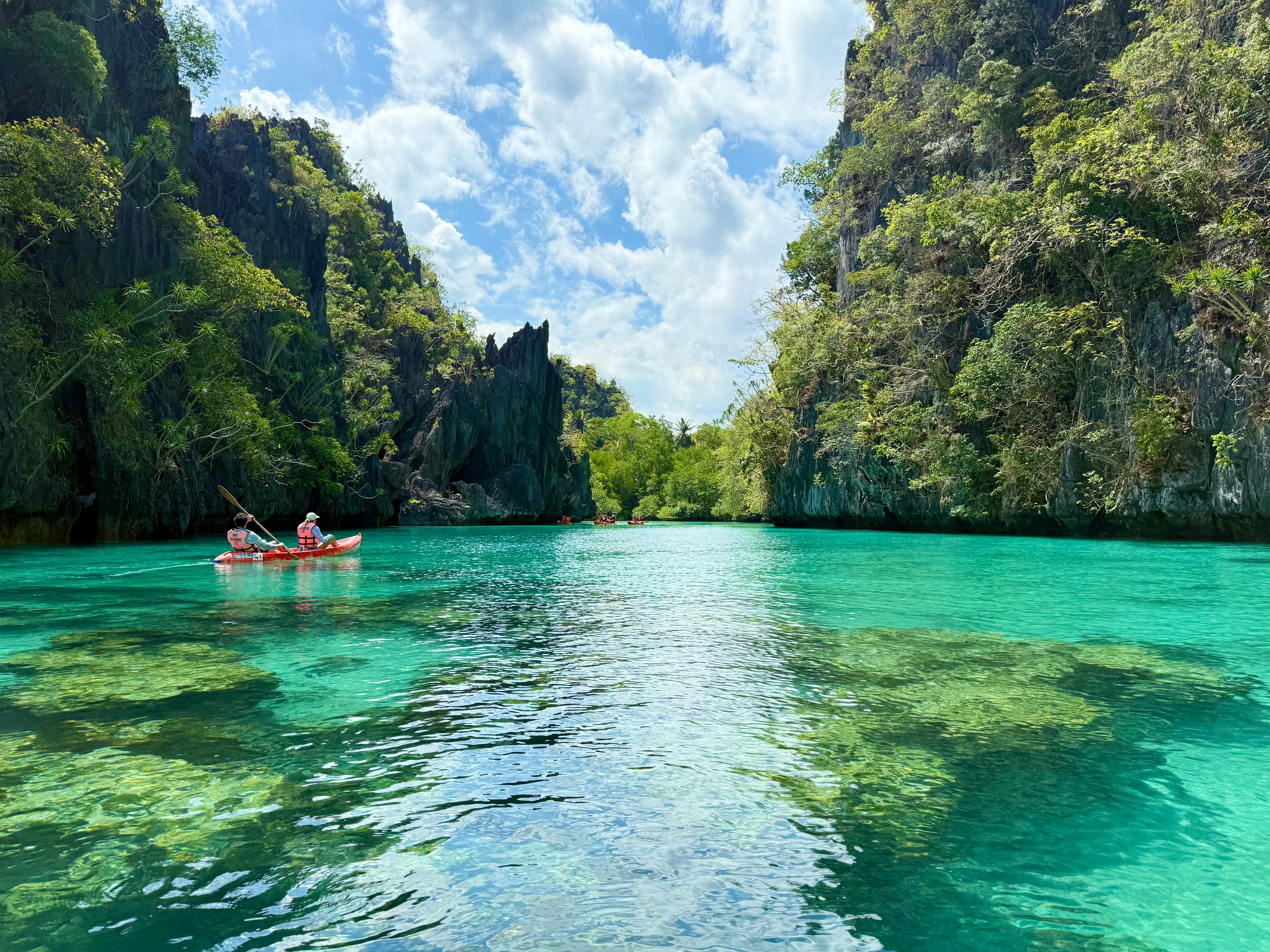 Kayakers explore a turquoise lagoon between cliffs.