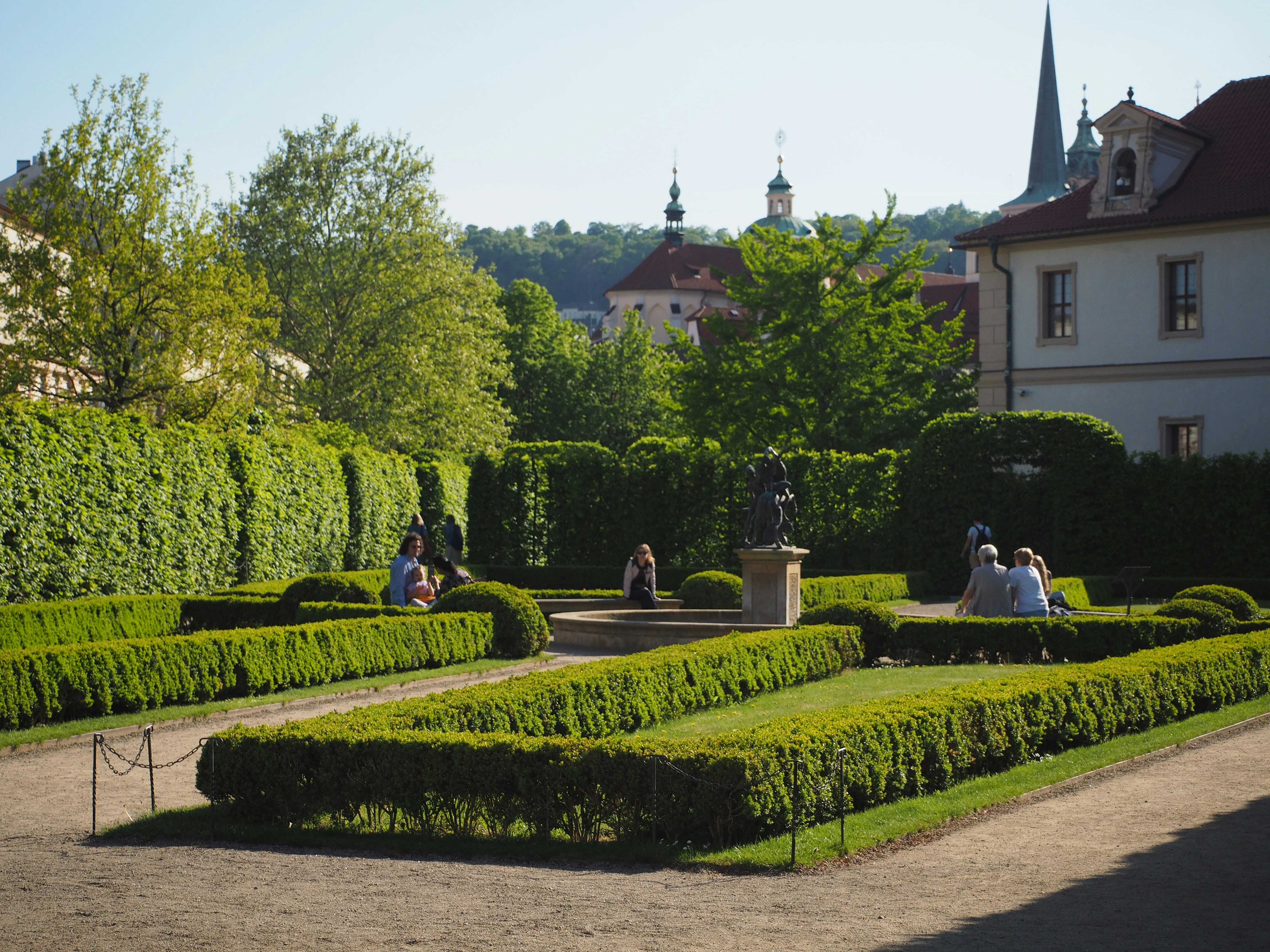 People relax in a manicured garden with a statue.
