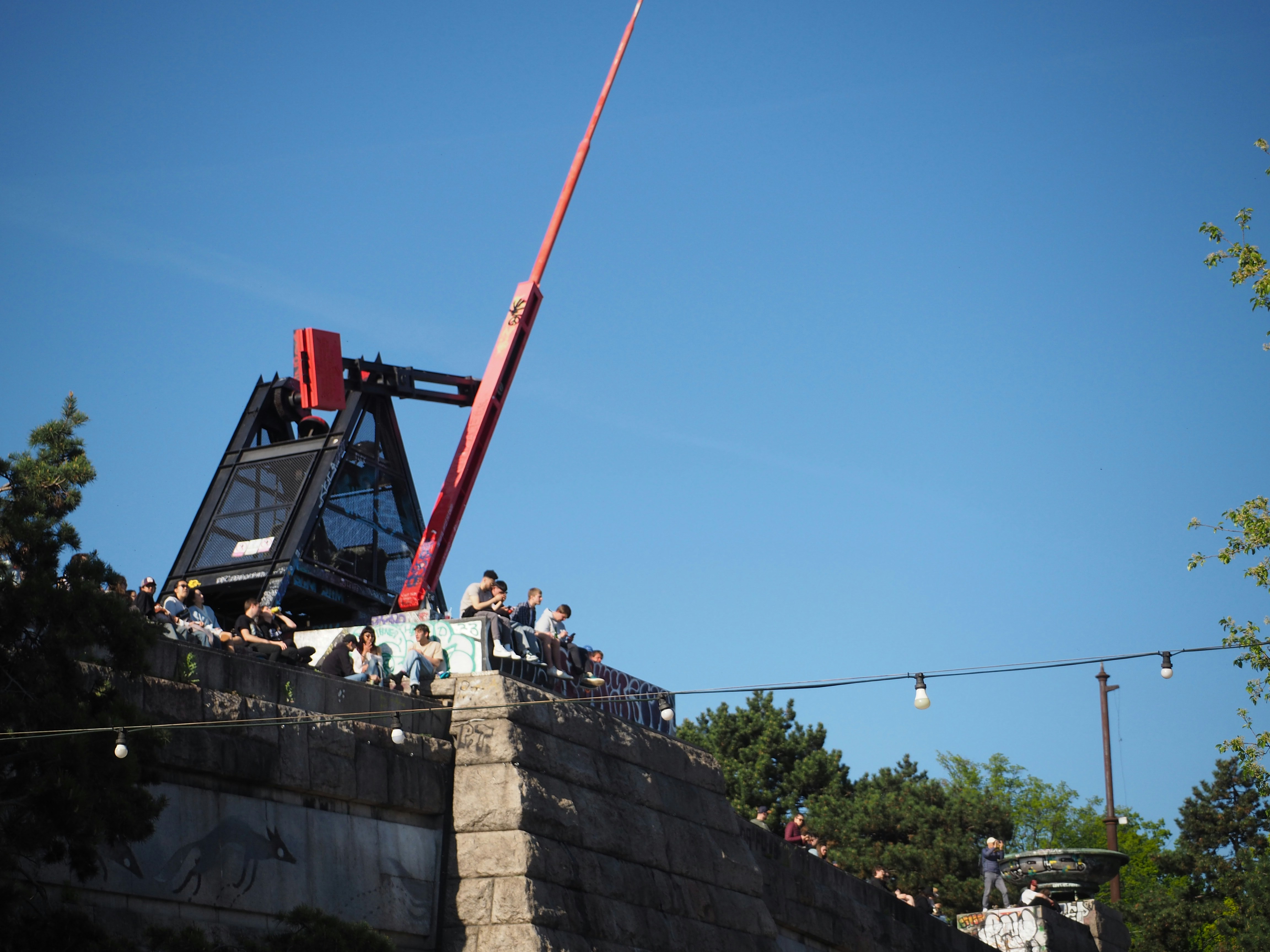 People sit near a structure with a red crane.