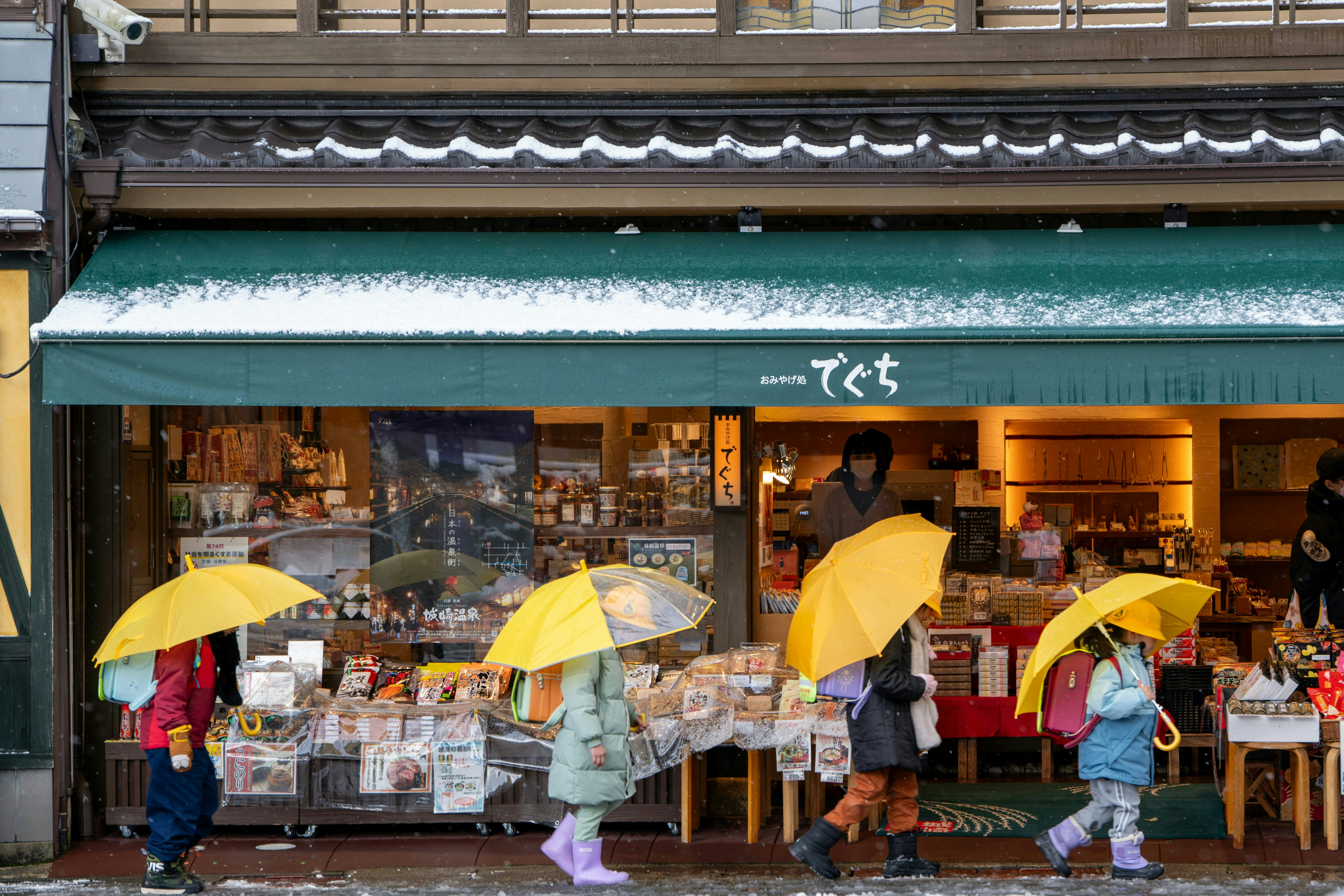 People with umbrellas walk past a shop.