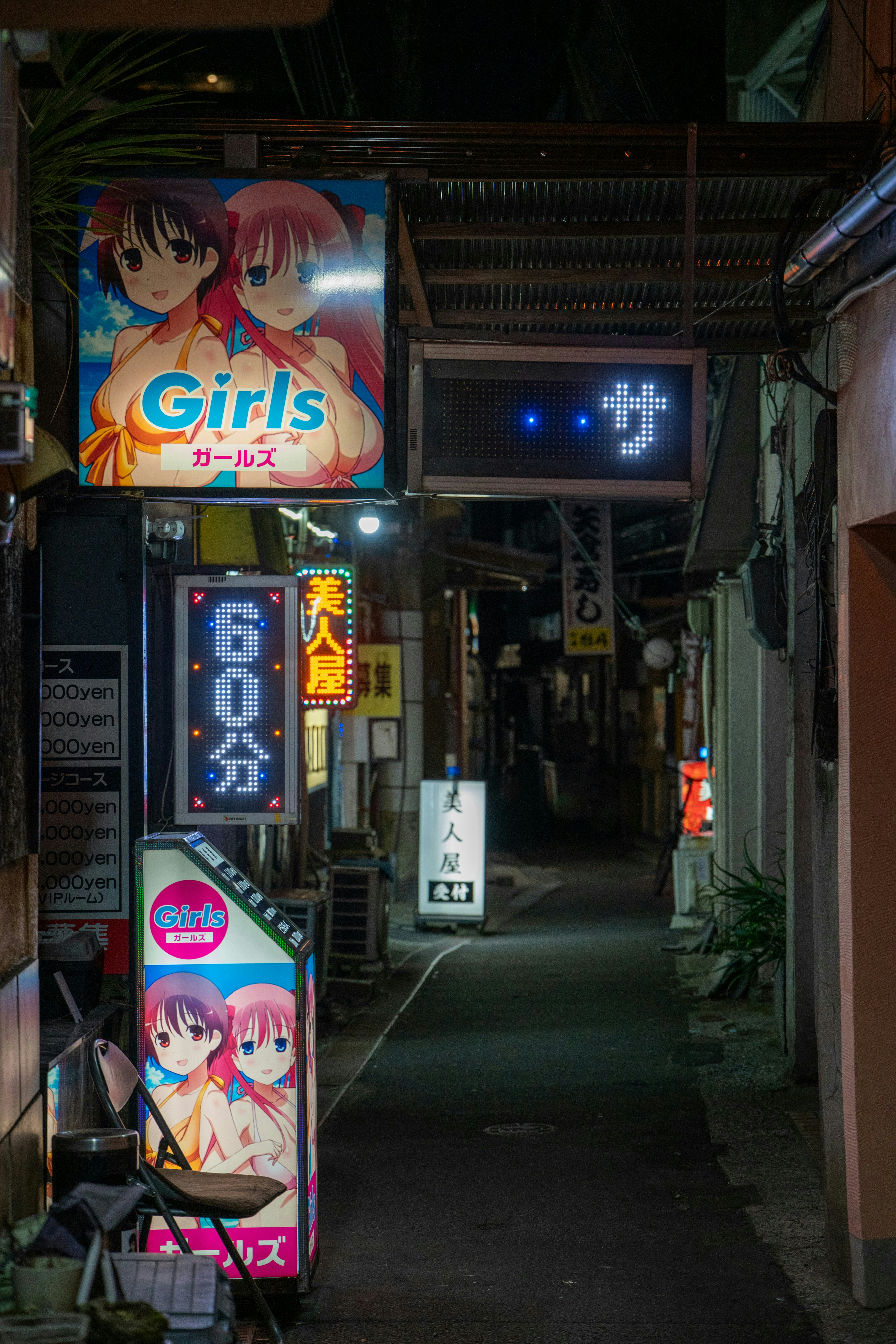Neon signs illuminate a dark alleyway in japan.
