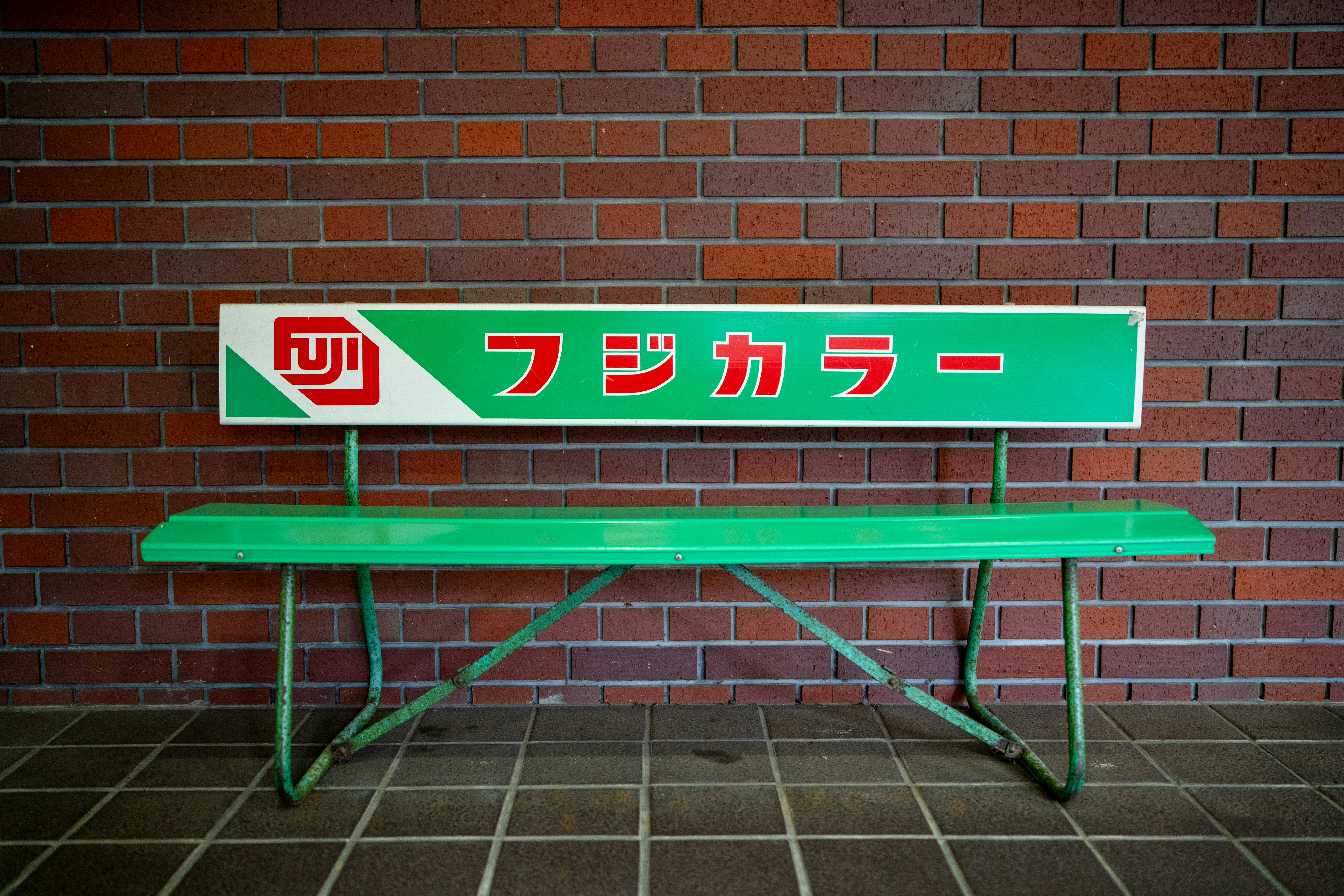 A fuji film bench sits in front of a brick wall.