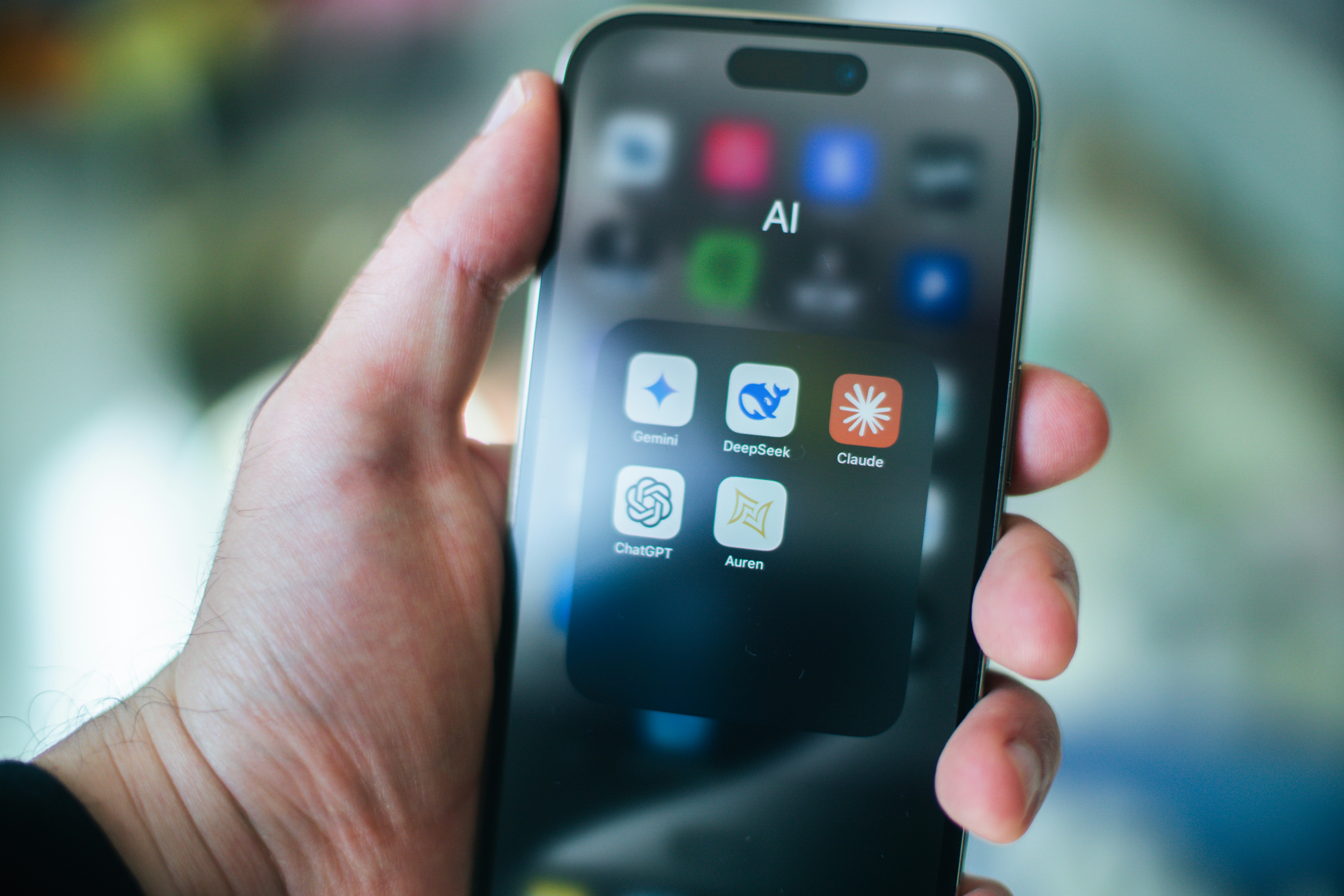 A hand holds a phone displaying apps.