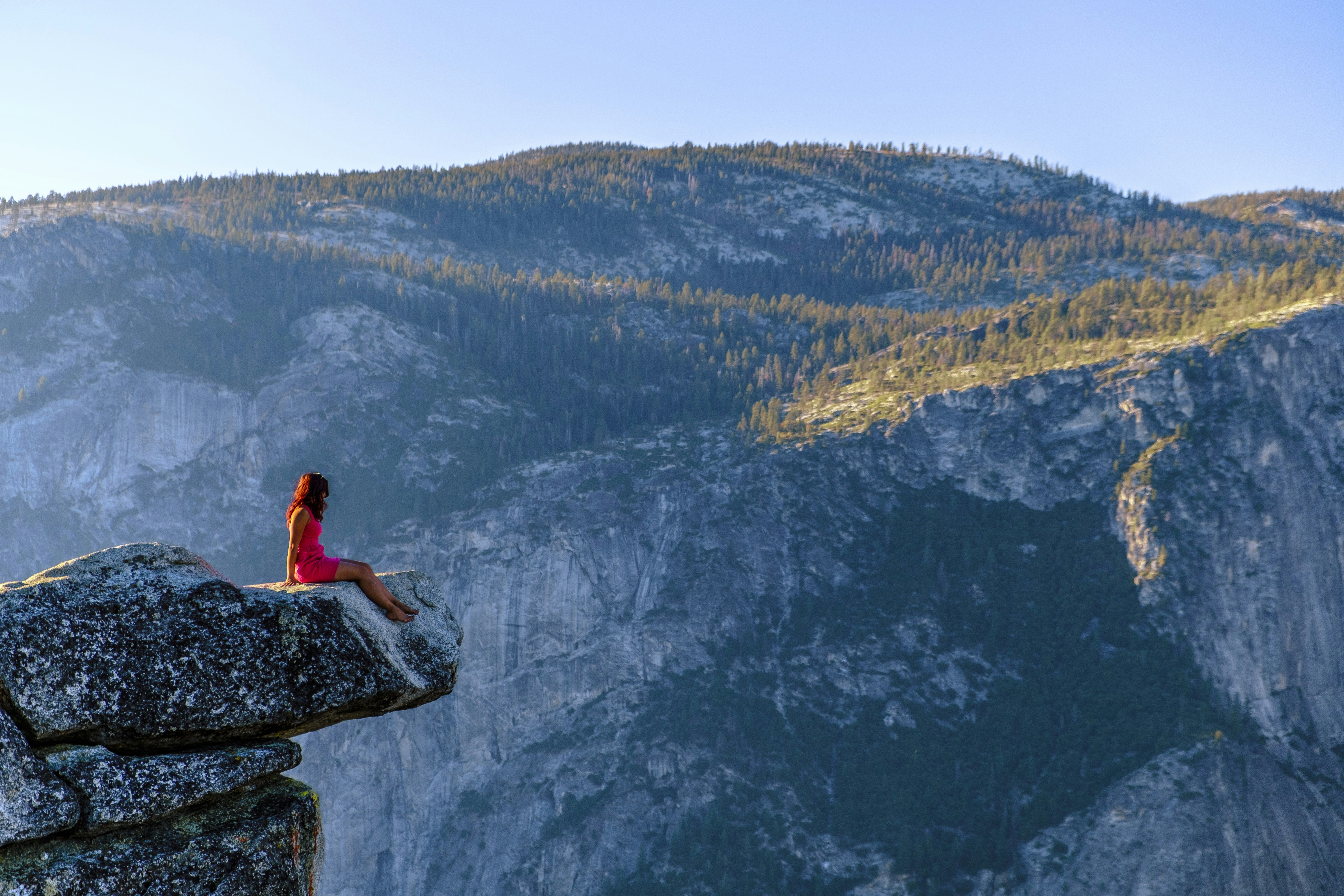 Woman sits on a cliff, overlooking mountains.