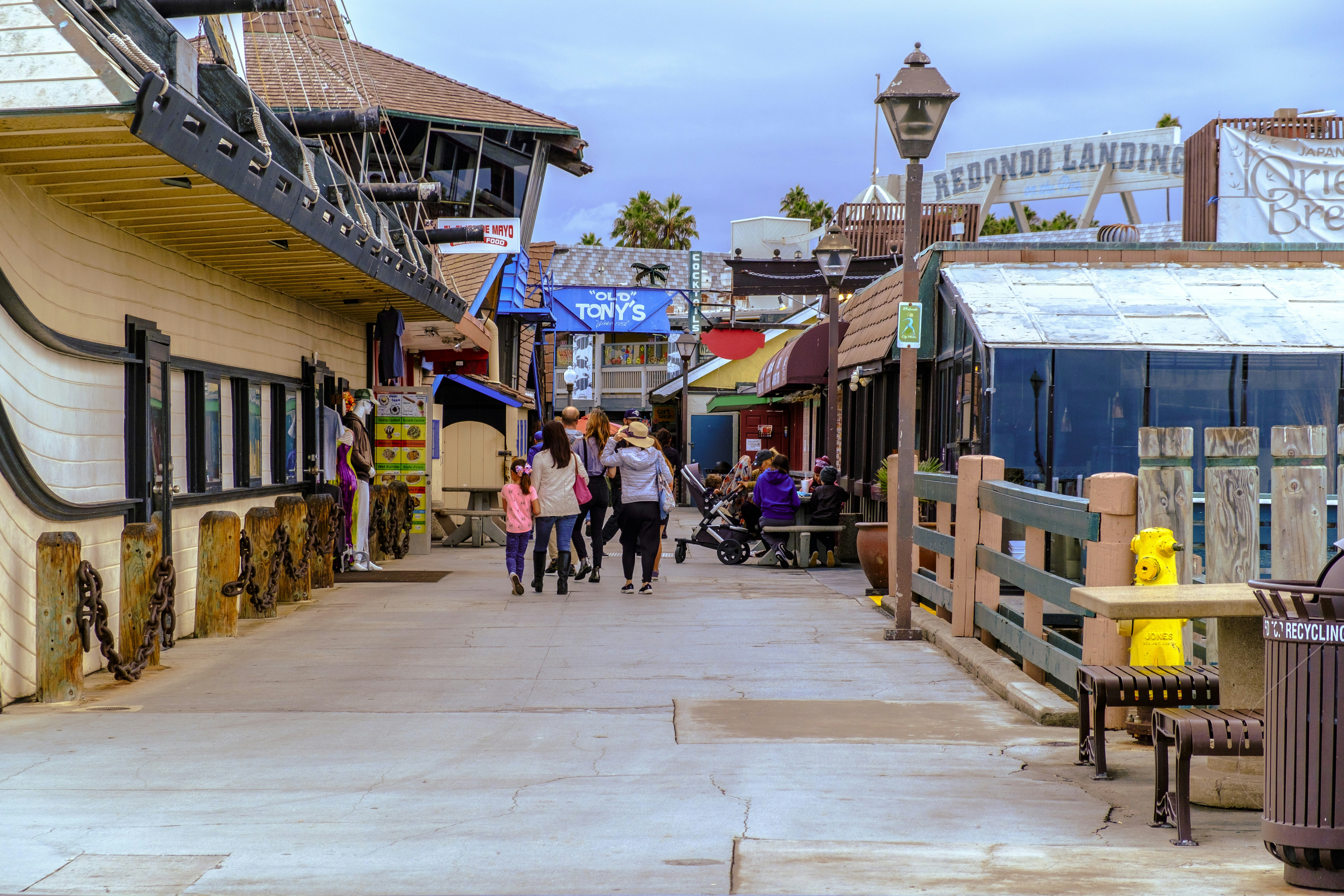 People stroll along a boardwalk with shops and restaurants.