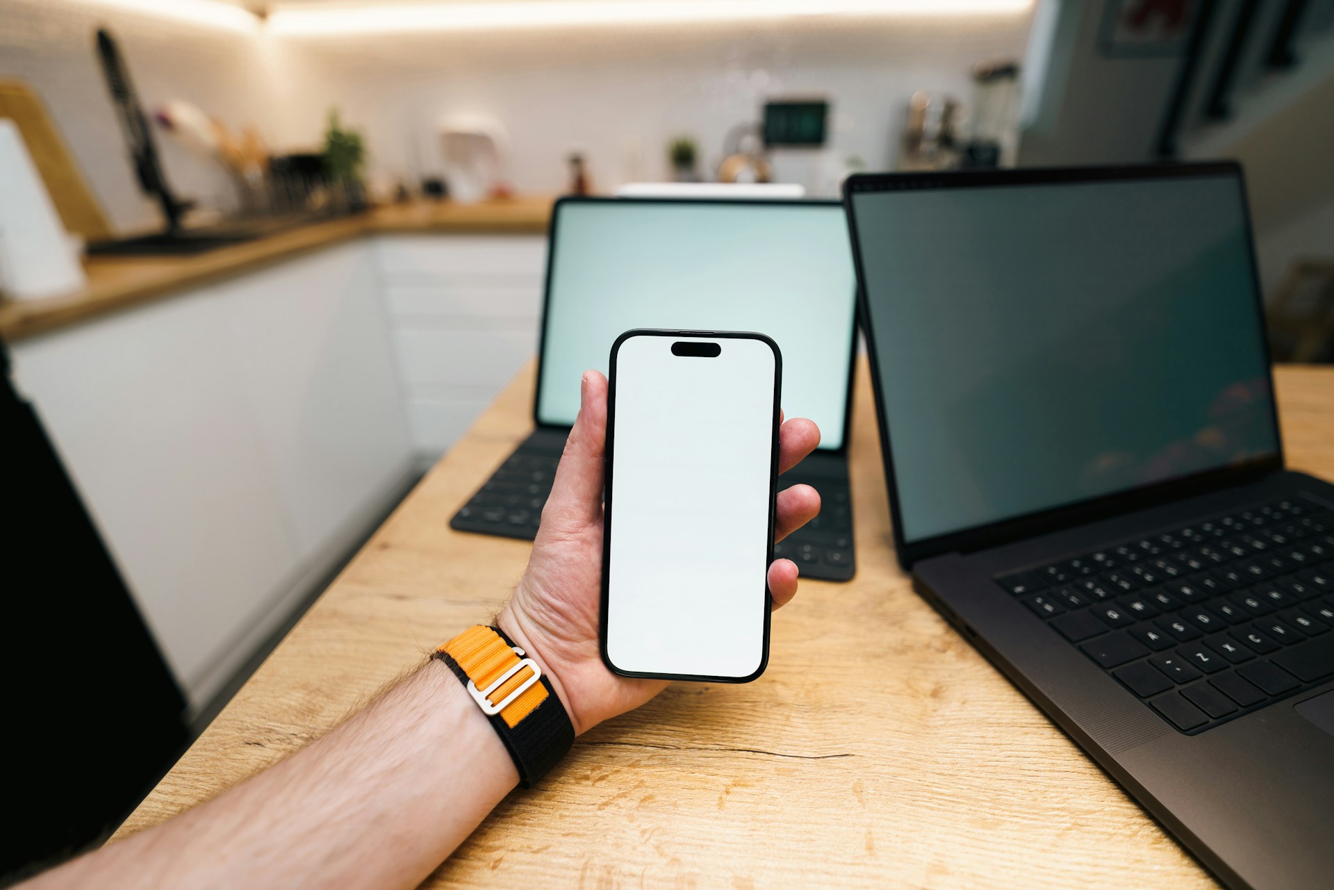 A hand holds a phone with two laptops behind it.