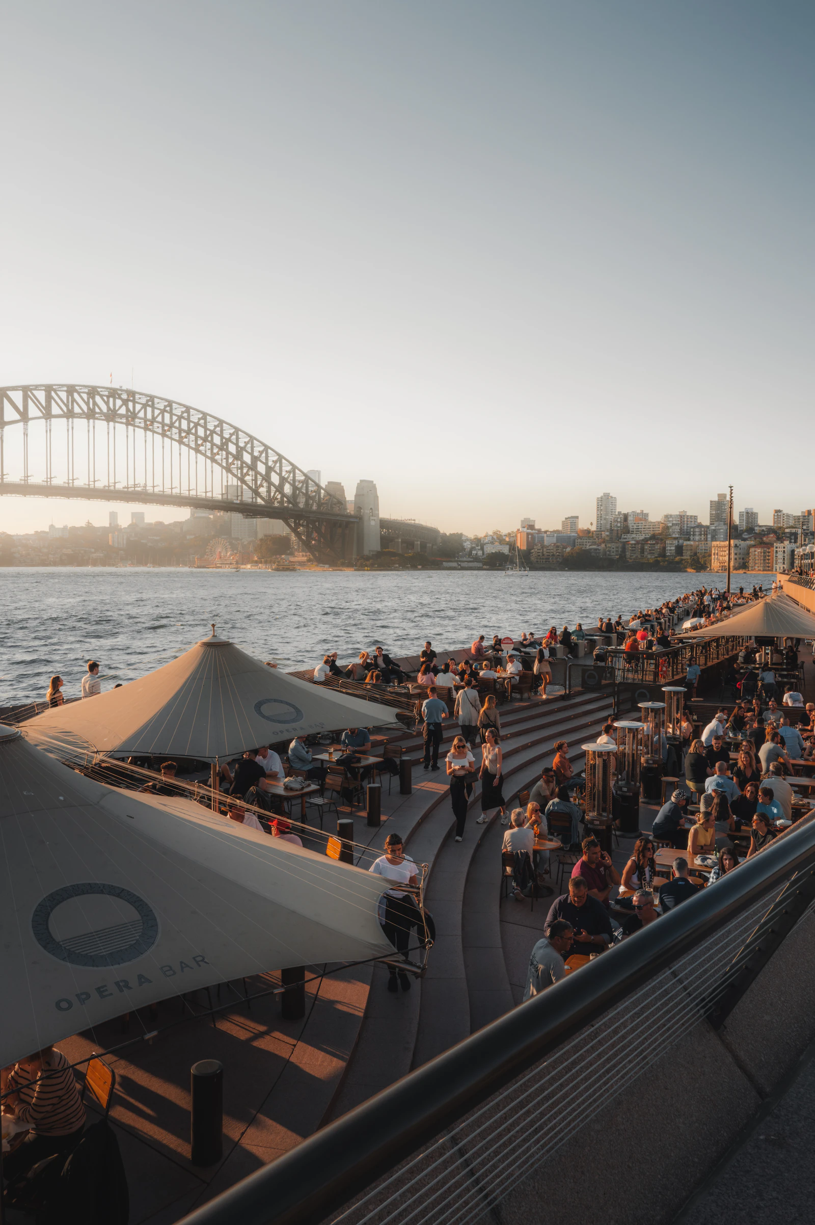 Young travellers at Opera Bar Sydney at golden hour, Harbour Bridge in the background