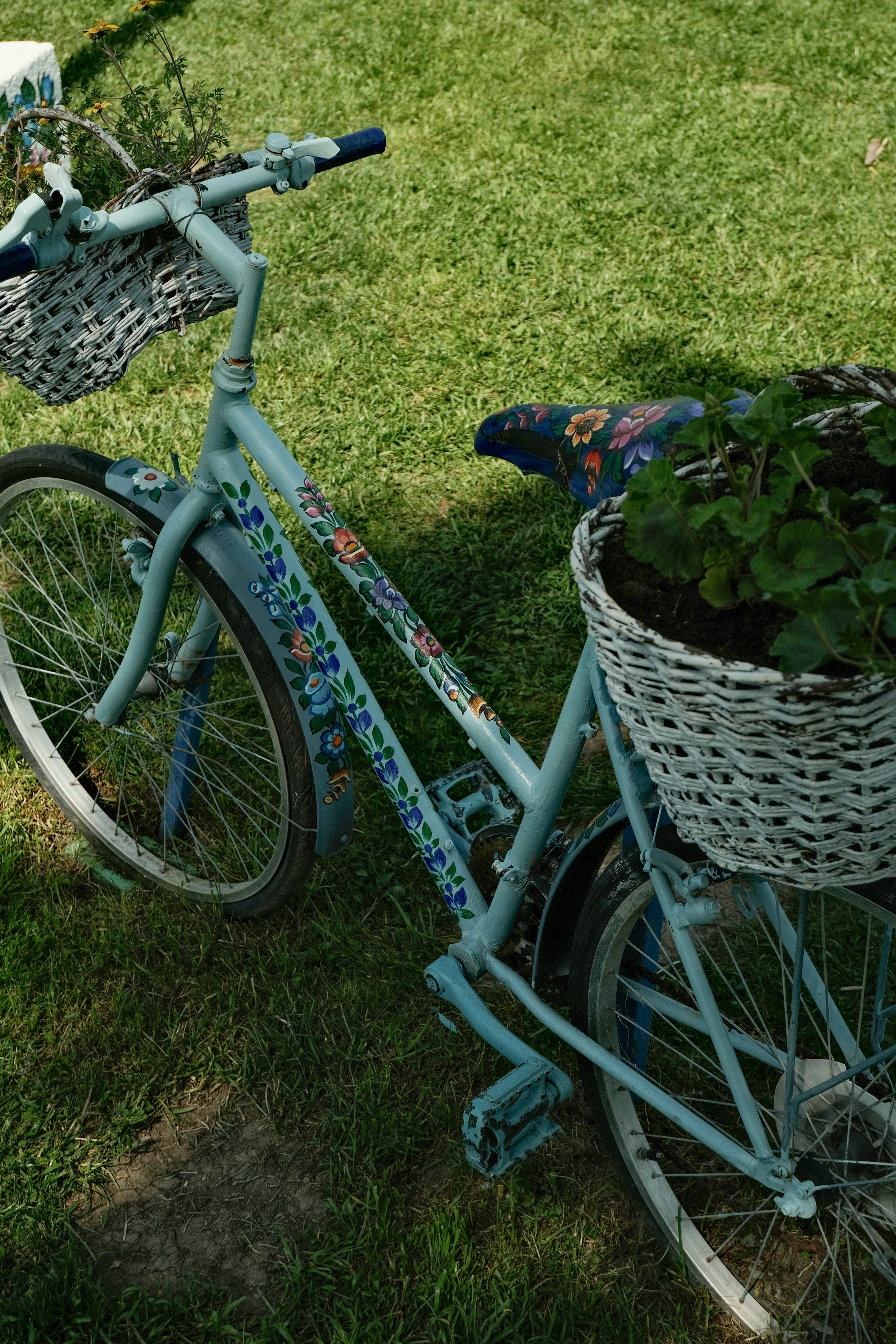 A floral decorated bike with baskets of plants.
