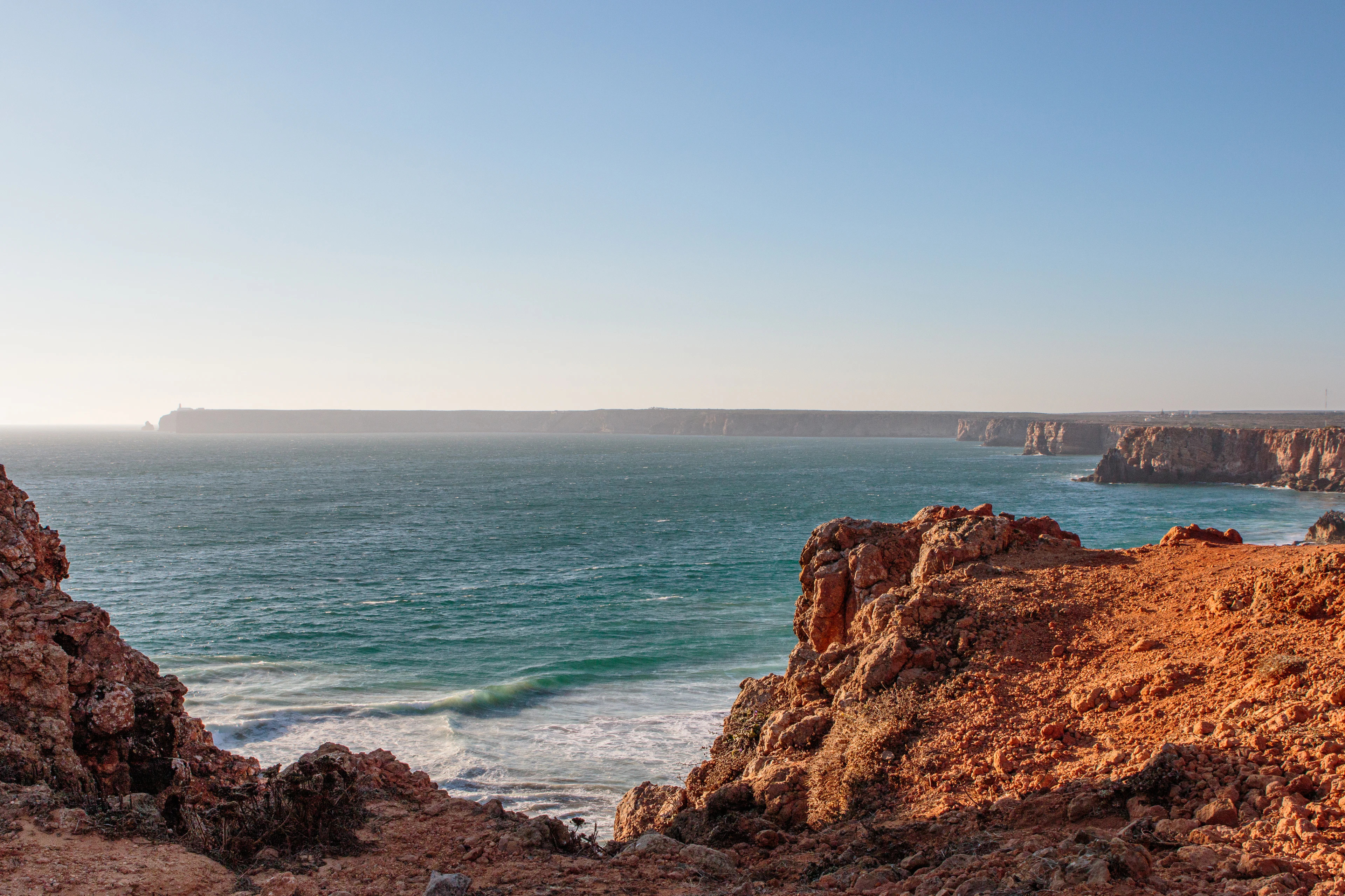 Golden-hour light over rugged sandstone cliffs stretching along the coastline to the horizon.