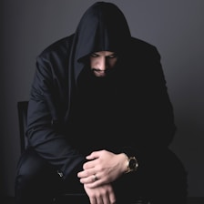 A person in a hood looks down, sitting.