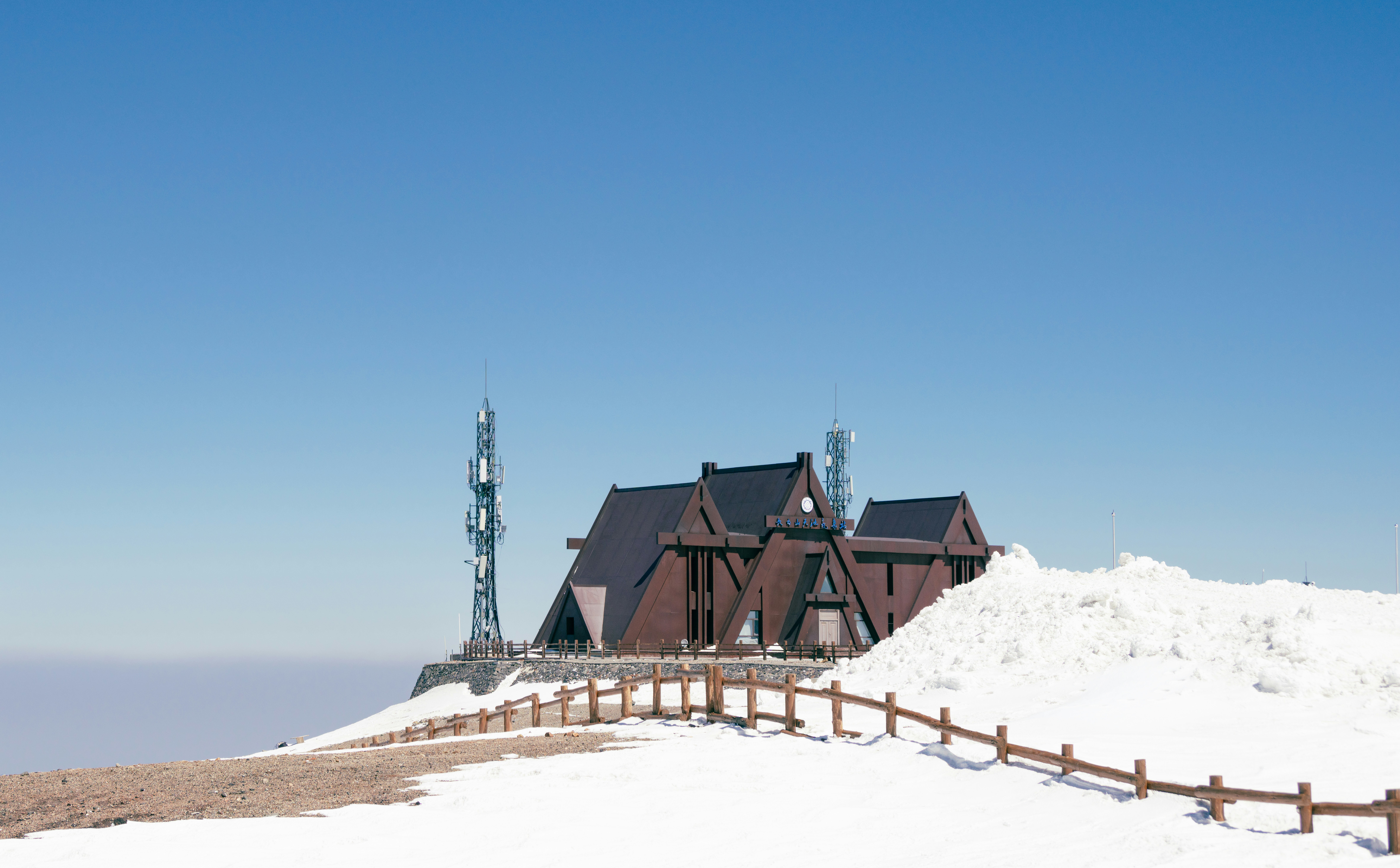 A wooden building on a snowy mountain under blue sky.