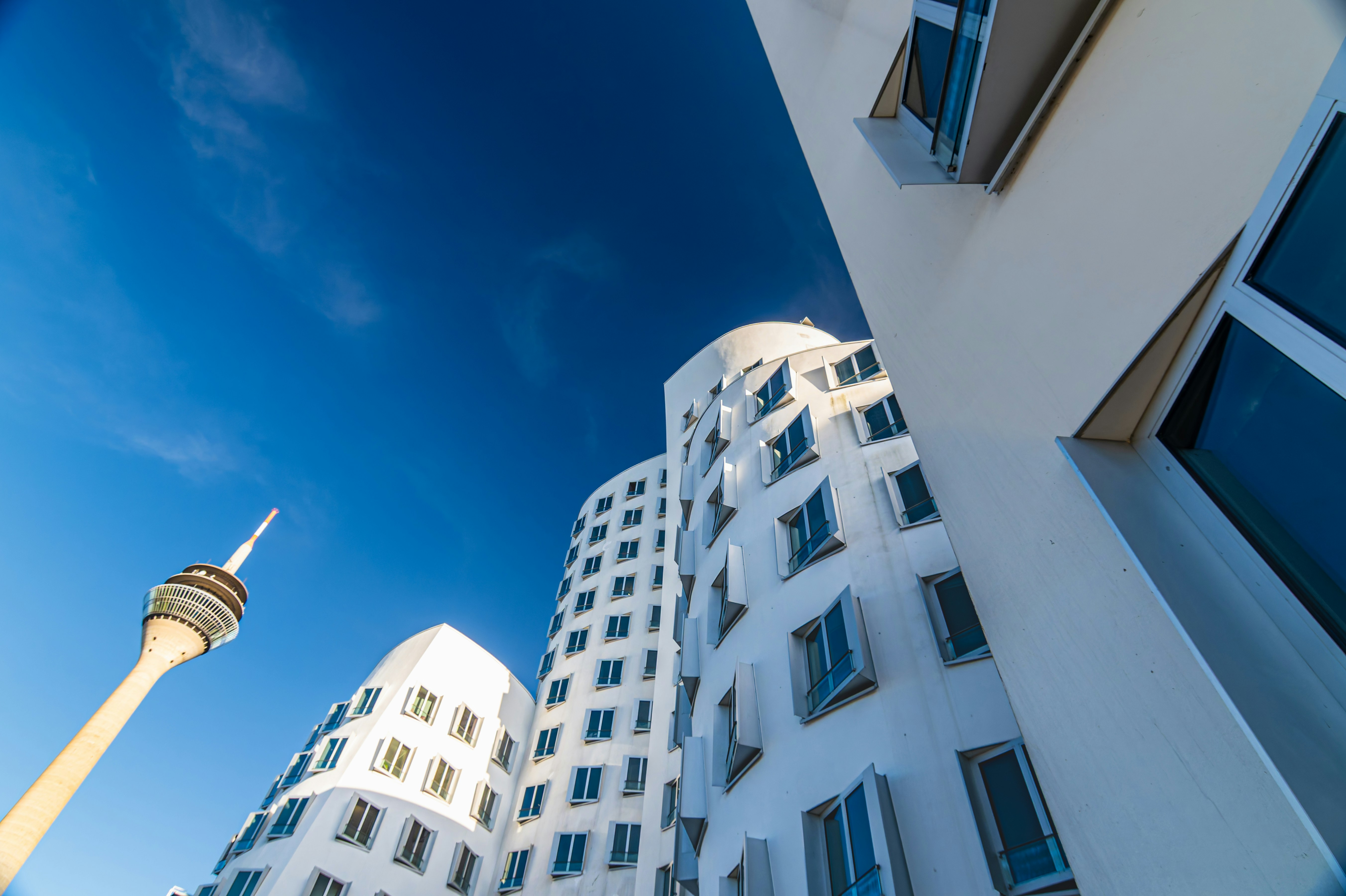 Modern architecture and a tall tower against blue sky.