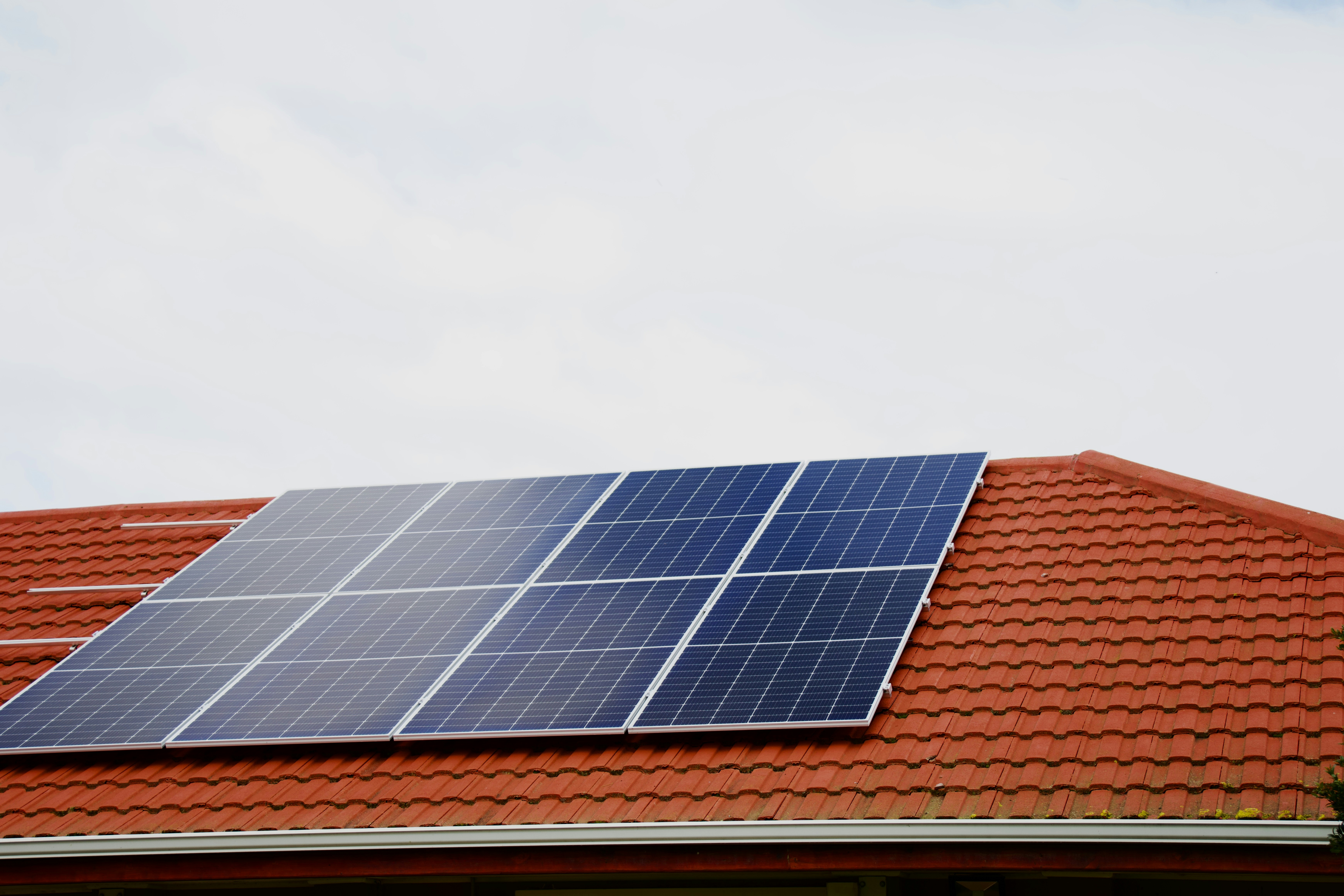 Blaue Solarmodule auf einem roten Ziegeldach eines Wohnhauses.