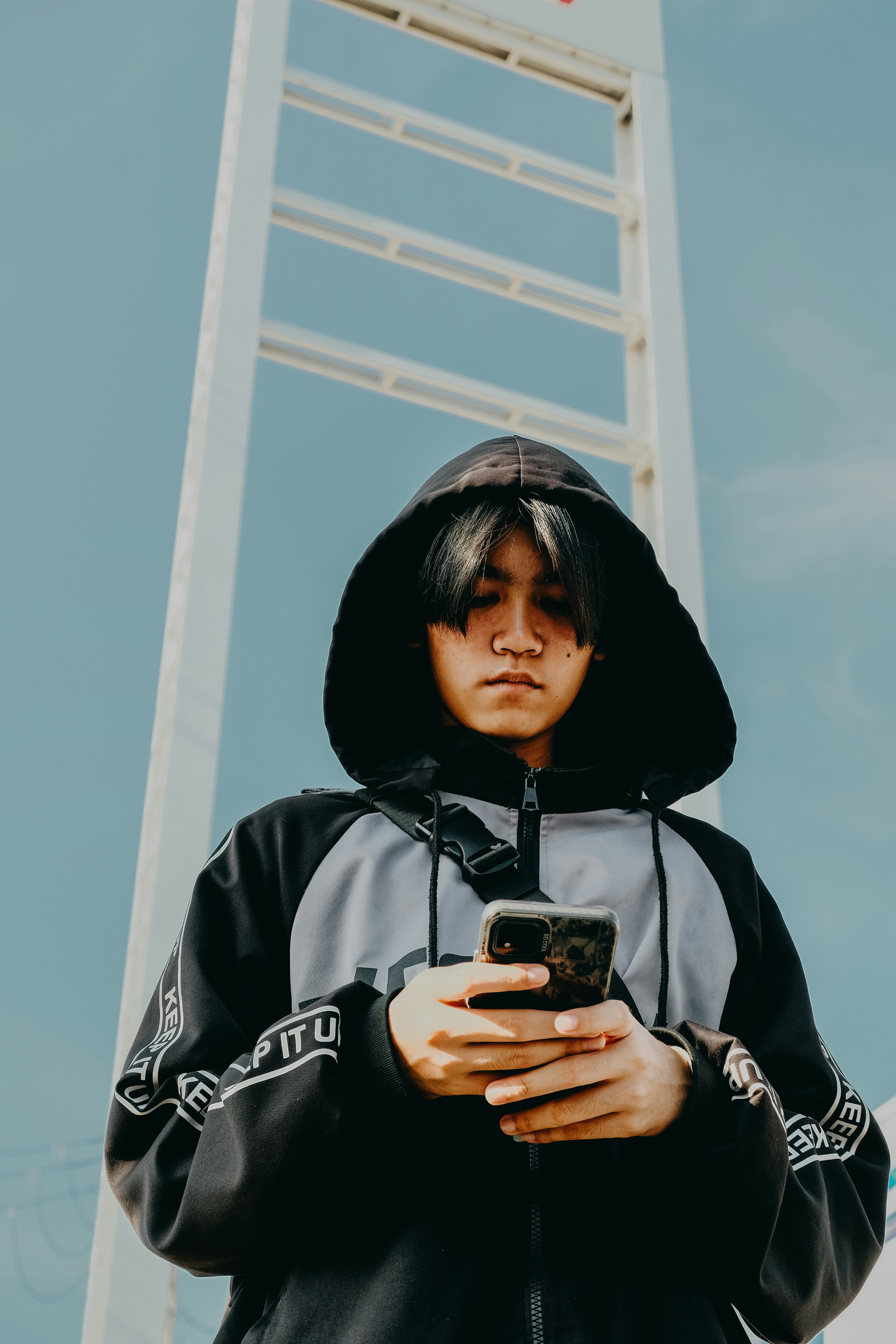 Pria muda yang mengenakan hoodie melihat ponselnya.
