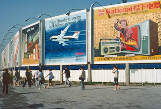 People walk past billboards with various advertisements.