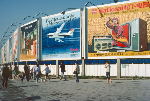 People walk past billboards with various advertisements.