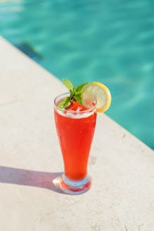 A refreshing drink sits by a swimming pool.