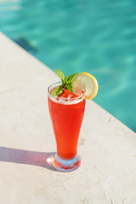 A refreshing drink sits by a swimming pool.