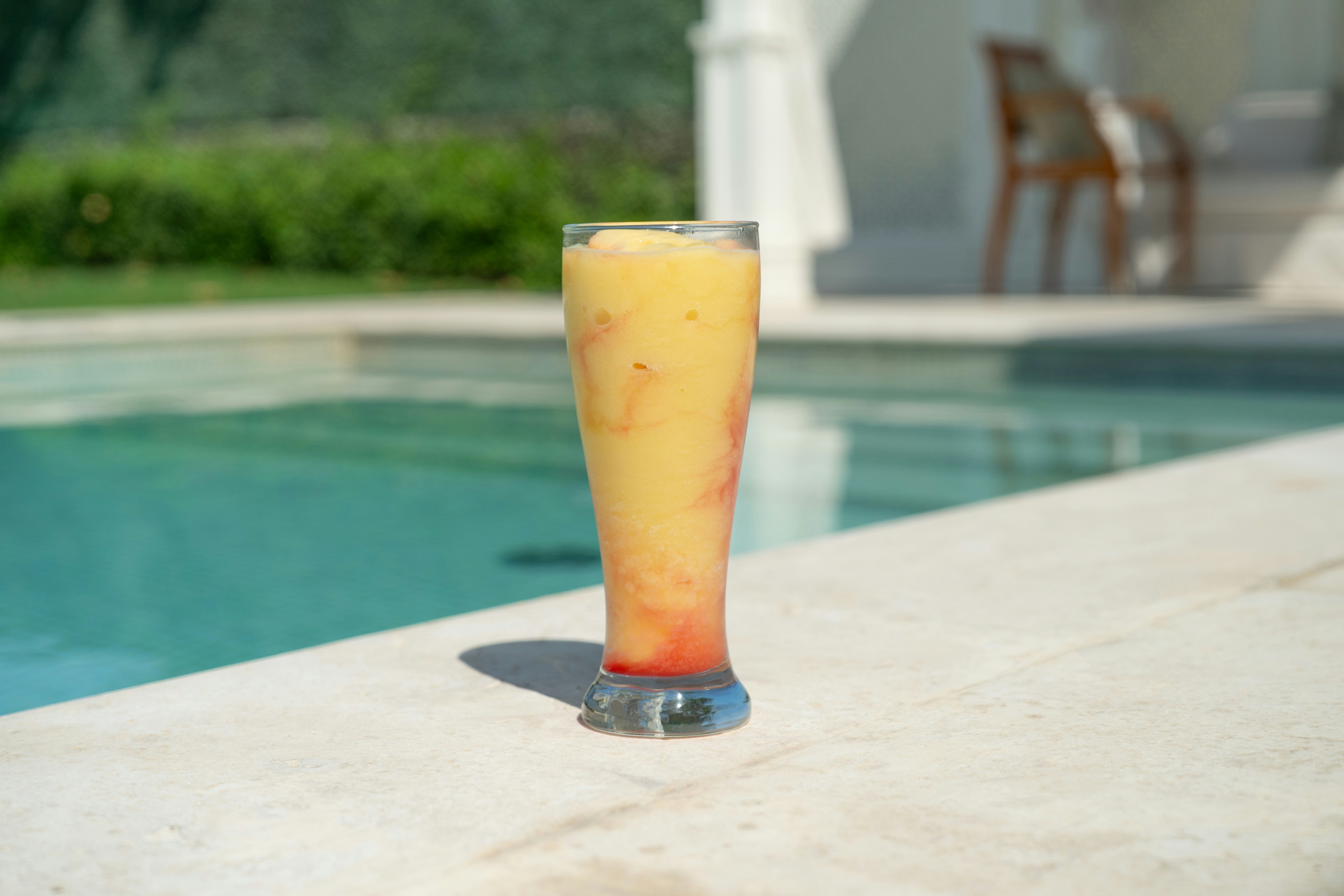 A colorful smoothie sits by a sparkling pool.