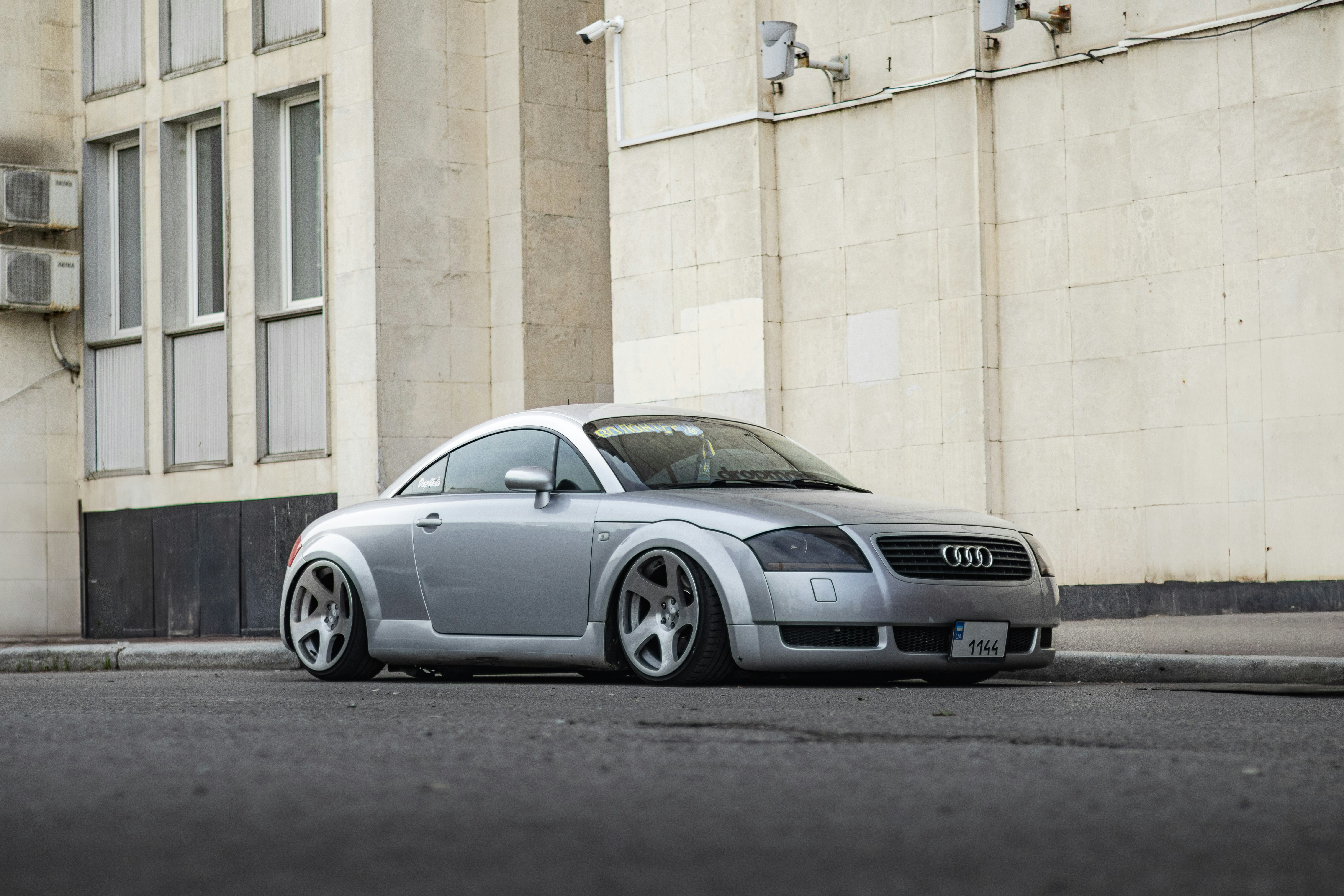 Here's a caption: silver audi tt sits parked on the street.