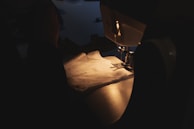 Someone sews with a sewing machine in dim light.