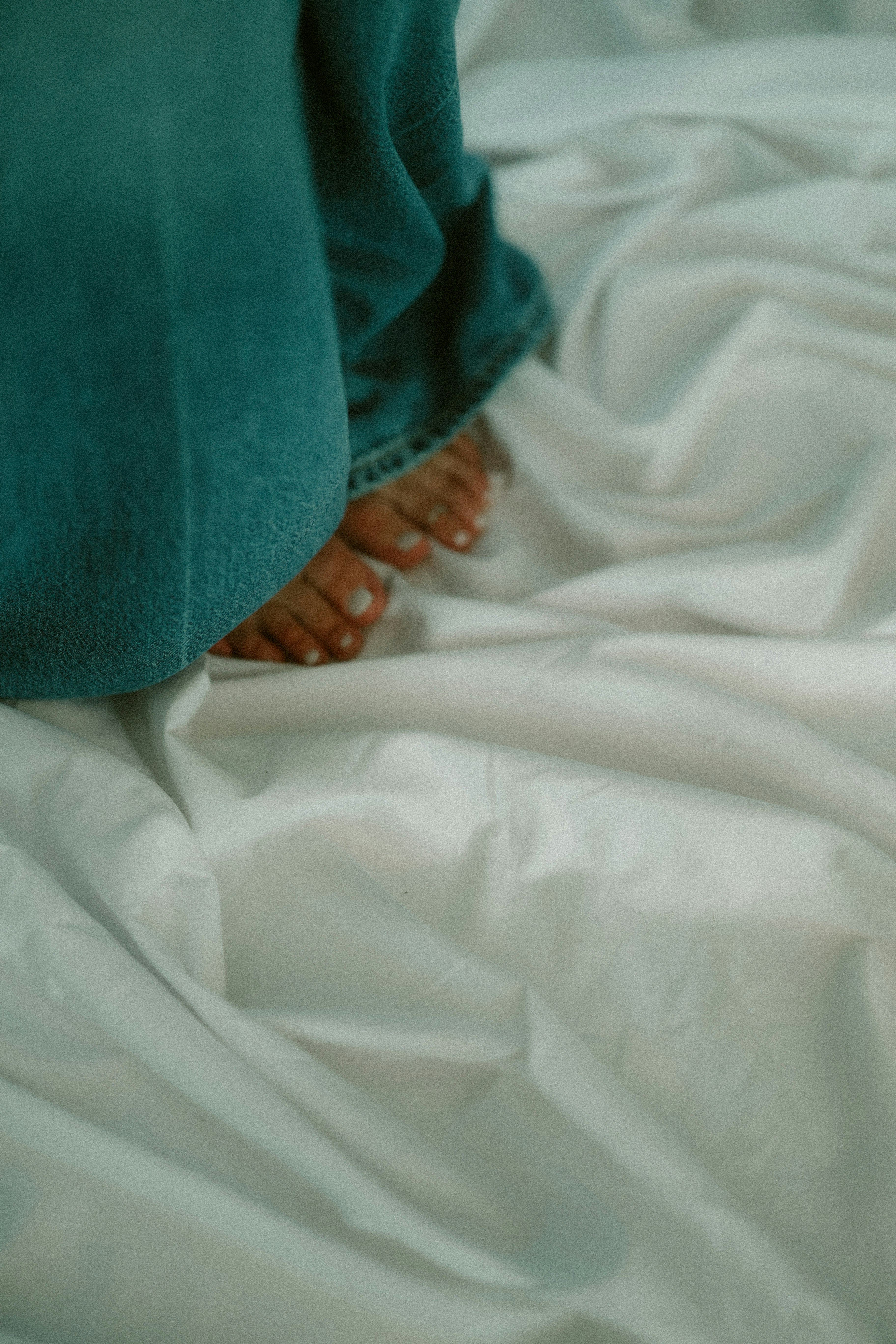 Bare feet rest on a rumpled white bed sheet.