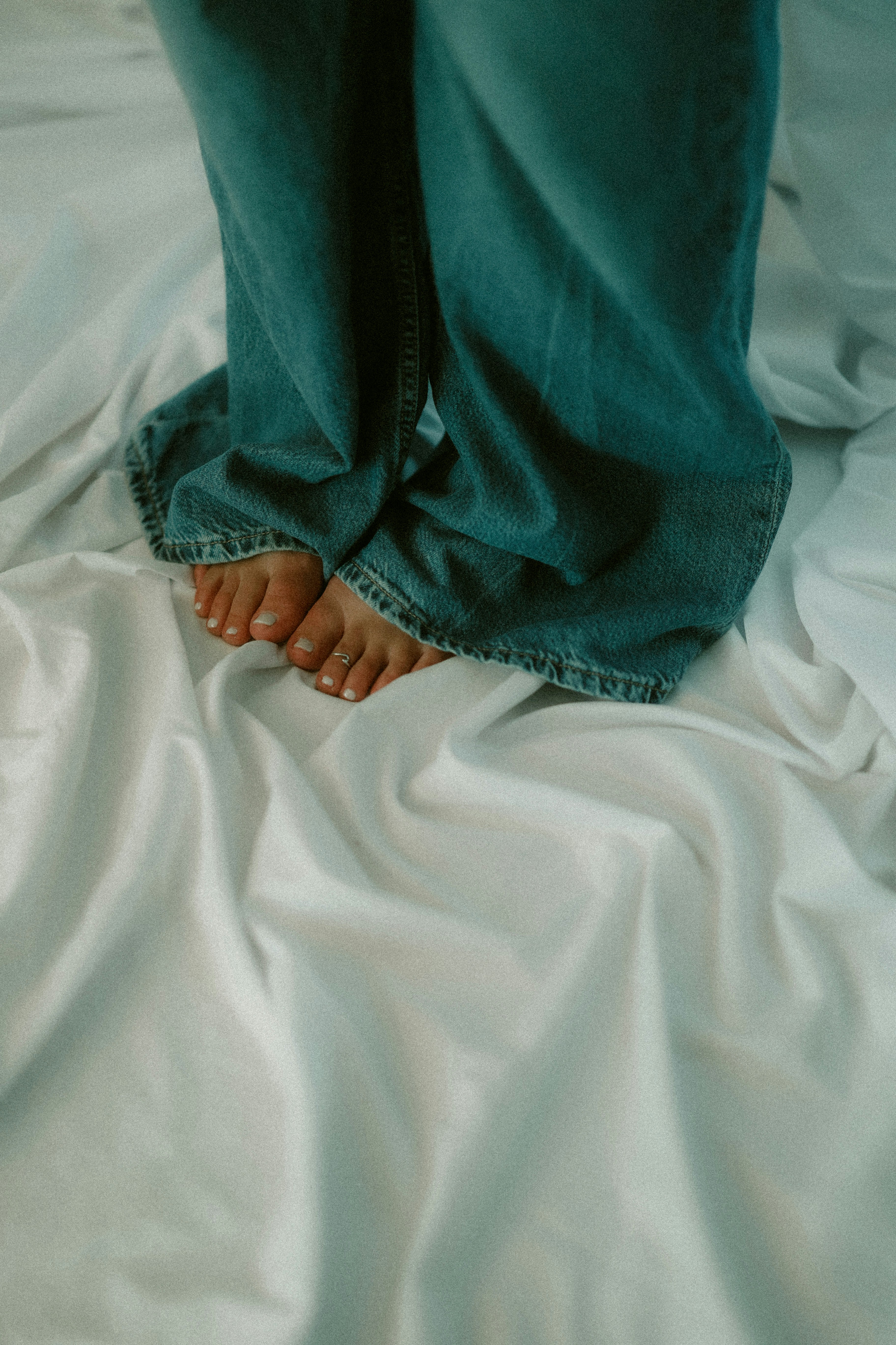 Feet and jeans stand on a rumpled white sheet.