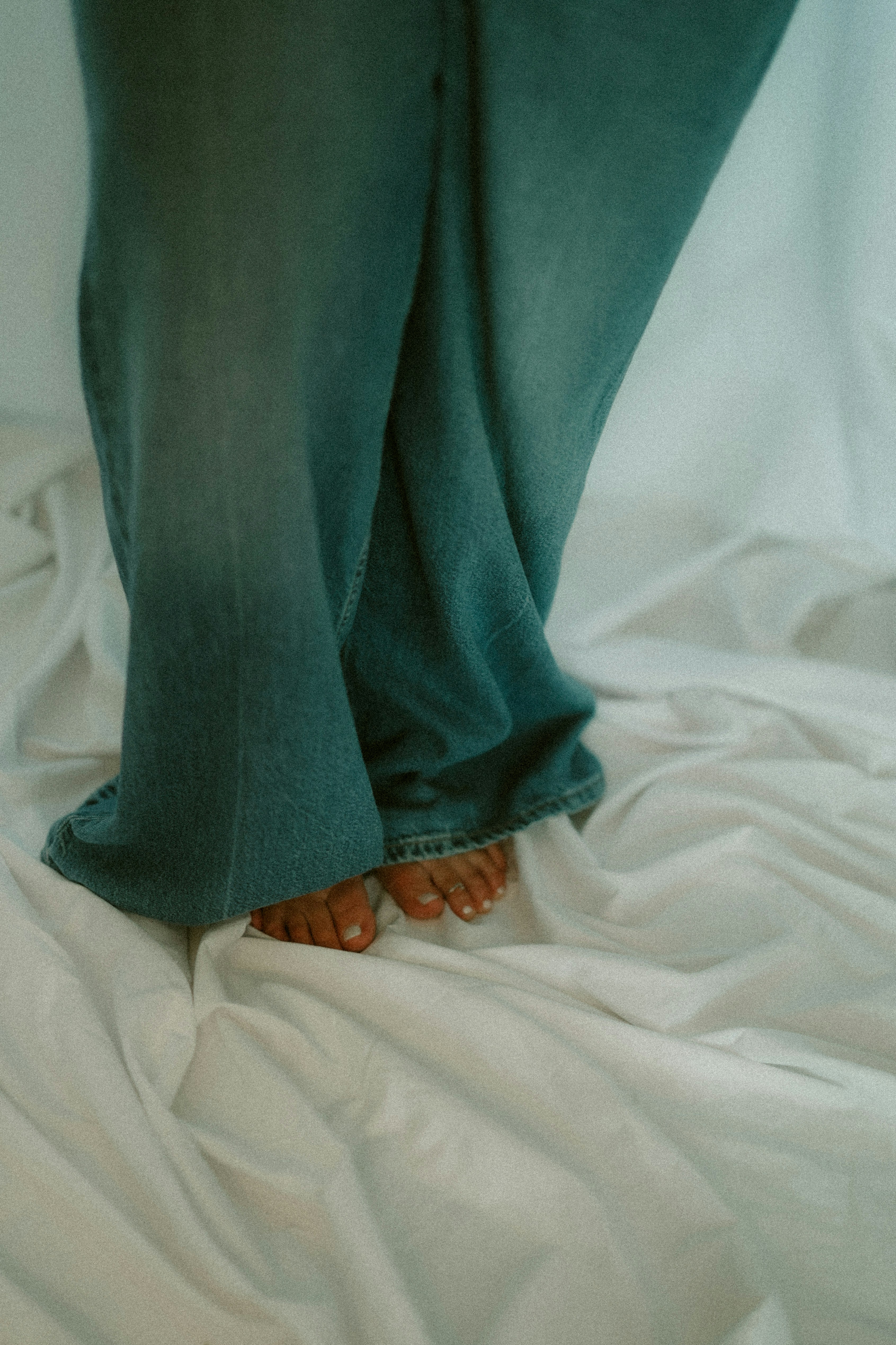 Bare feet in jeans on a wrinkled white sheet.