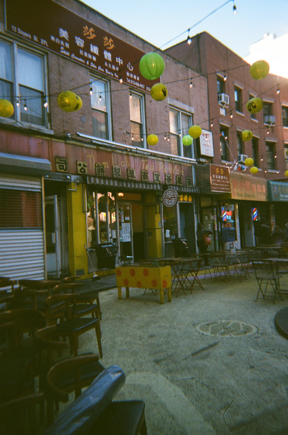 Nom Wah Tea Parlor on Doyers Street in Manhattan's Chinatown: red lanterns strung above a curved historic street with brick tenement buildings and dim sum awnings