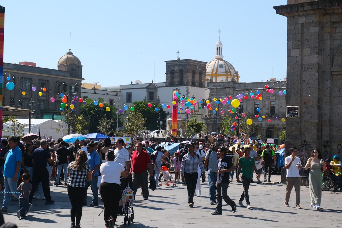 People gather in a sunny plaza with colorful balloons