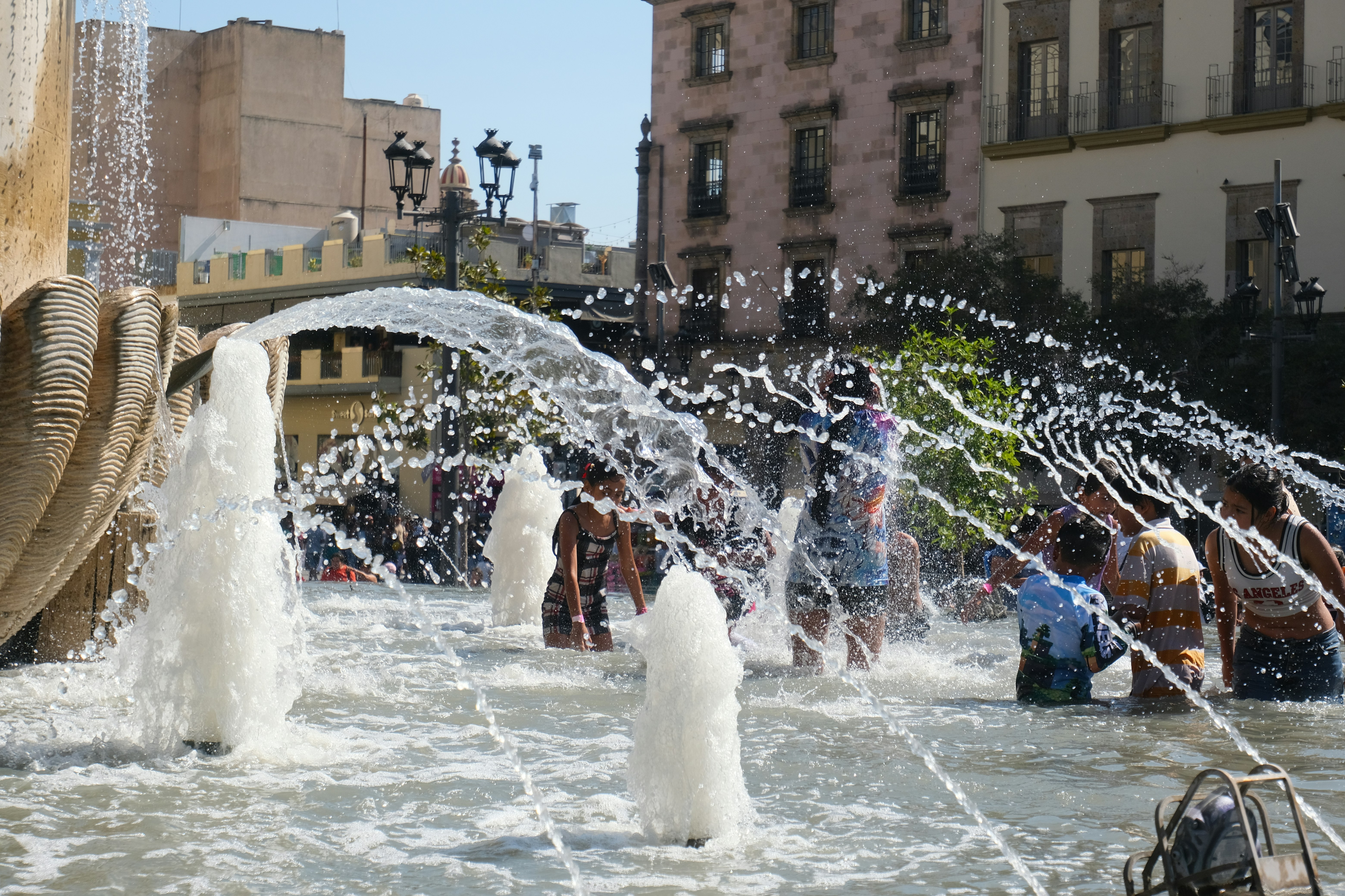 People enjoy a fountain on a hot day.