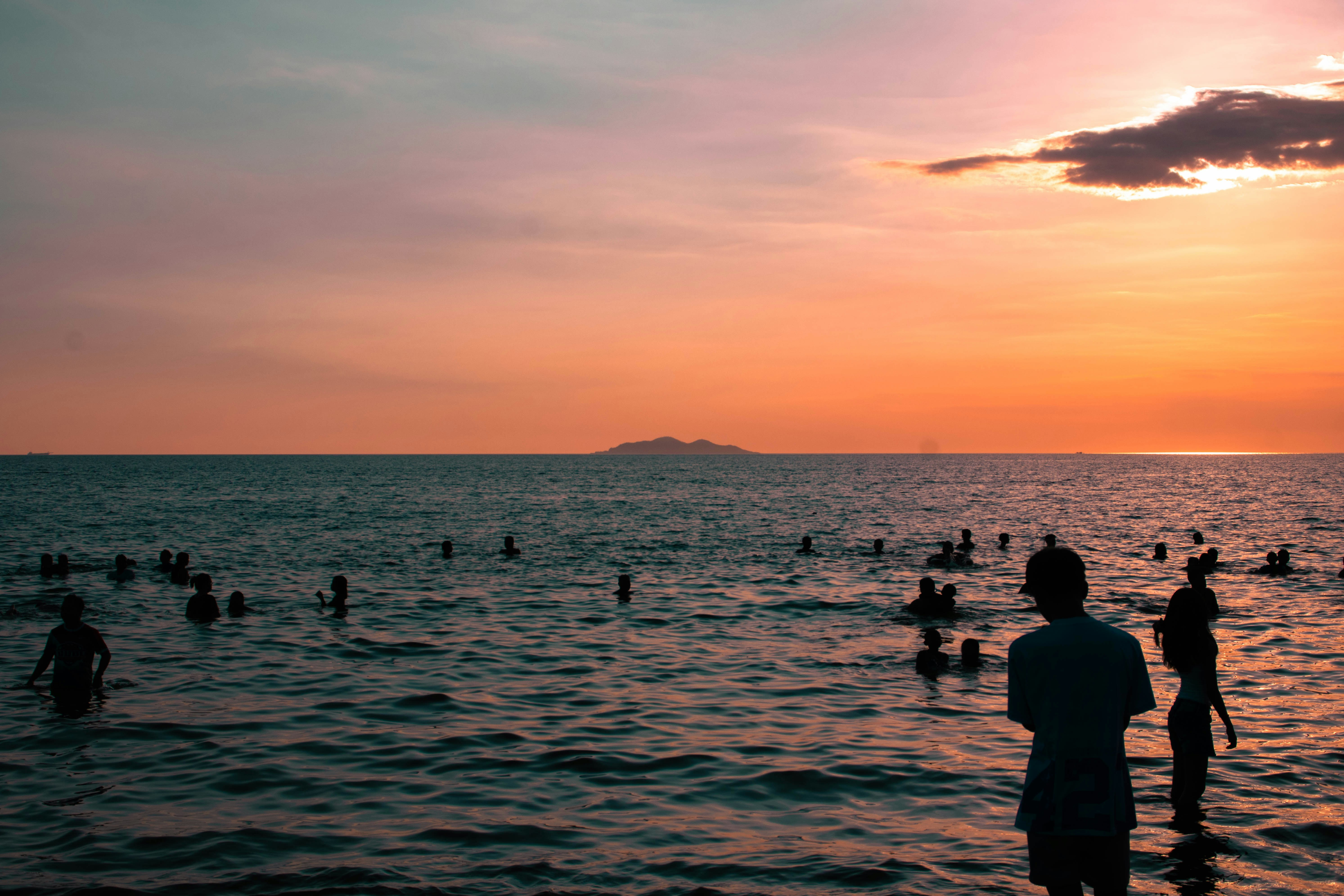 People swim in the ocean during a sunset.
