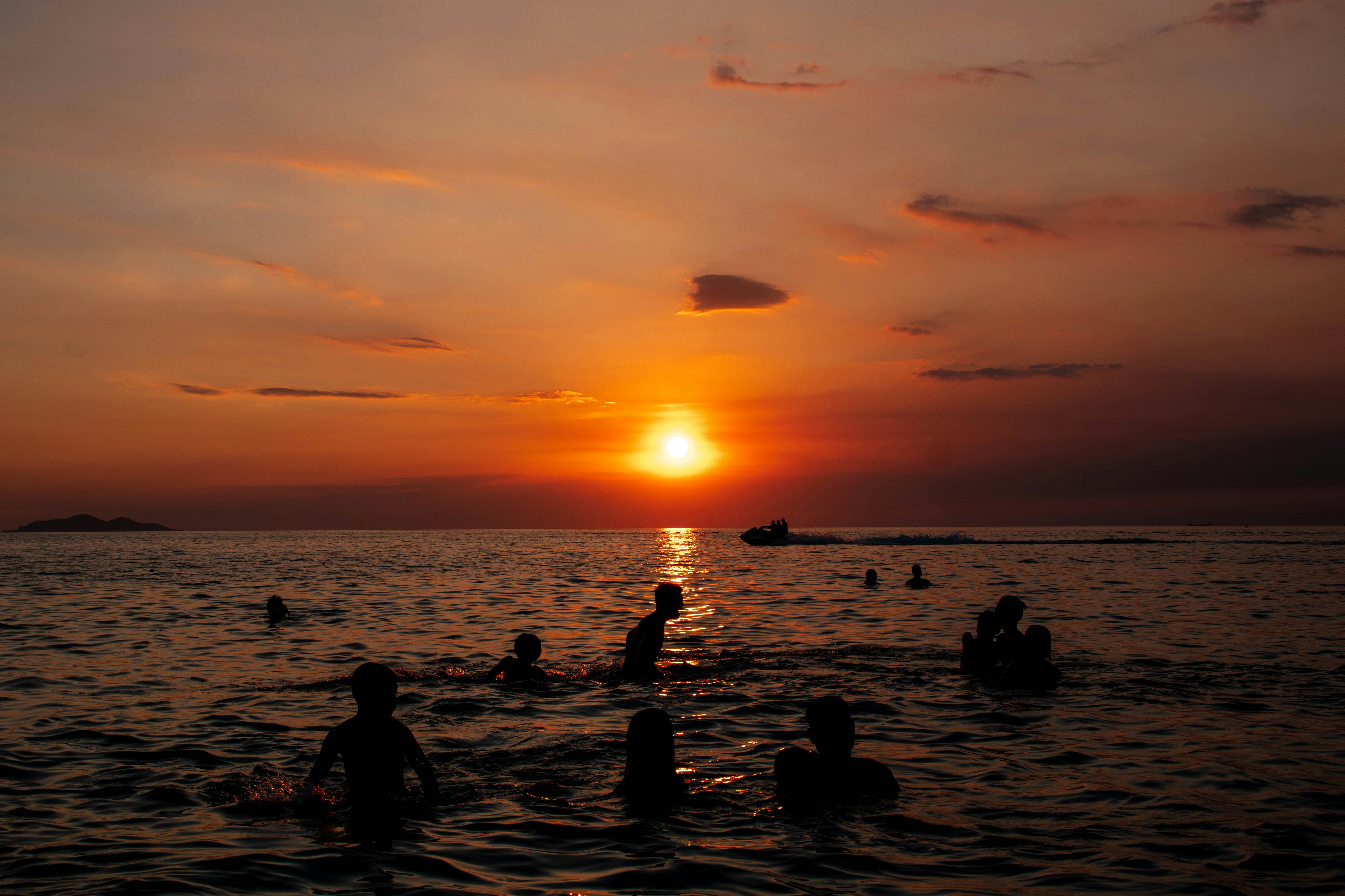 Sunset silhouettes people swimming in the ocean.