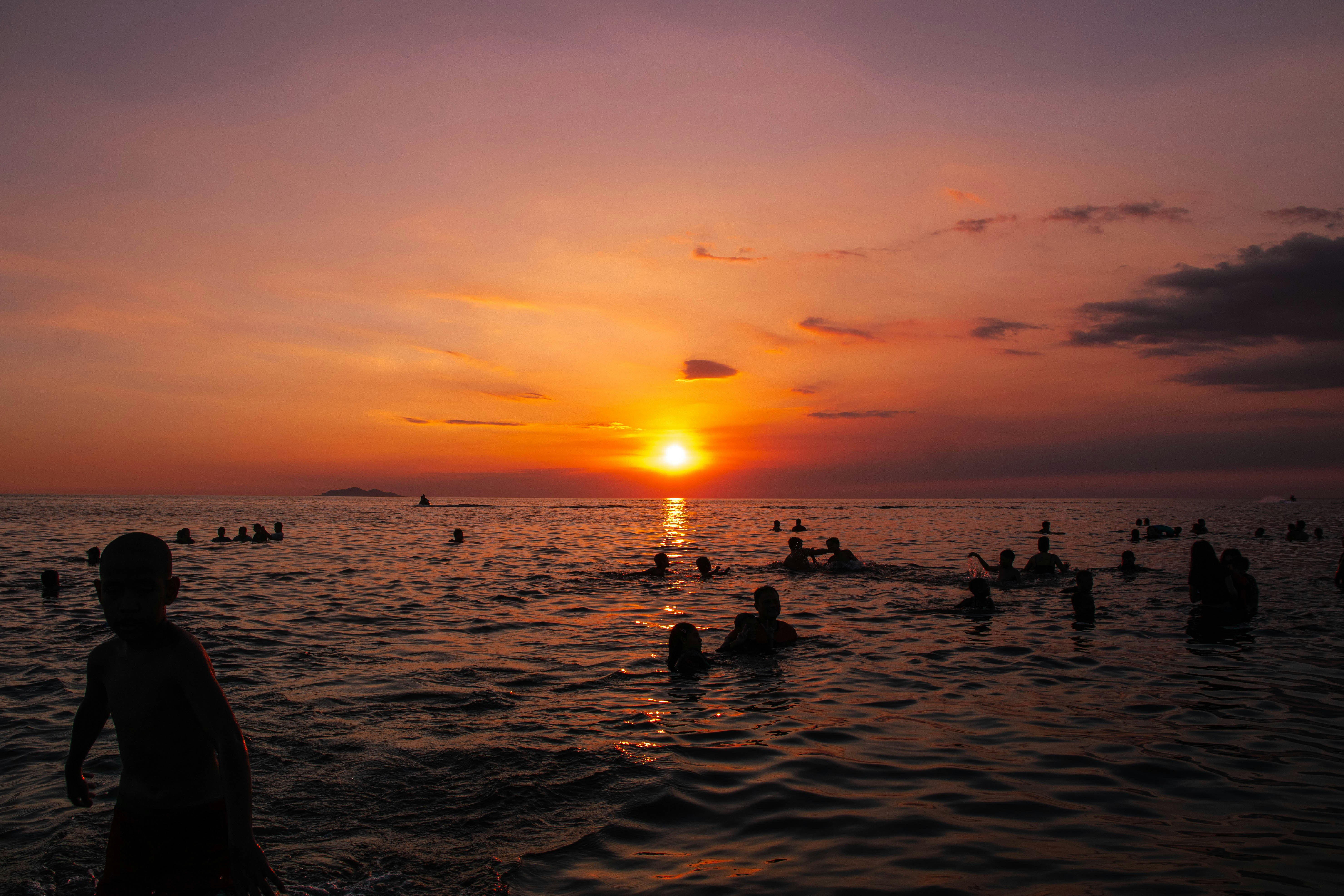 People swim as the sun sets over the ocean.