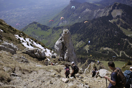 Hikers trek near paragliders in a scenic landscape