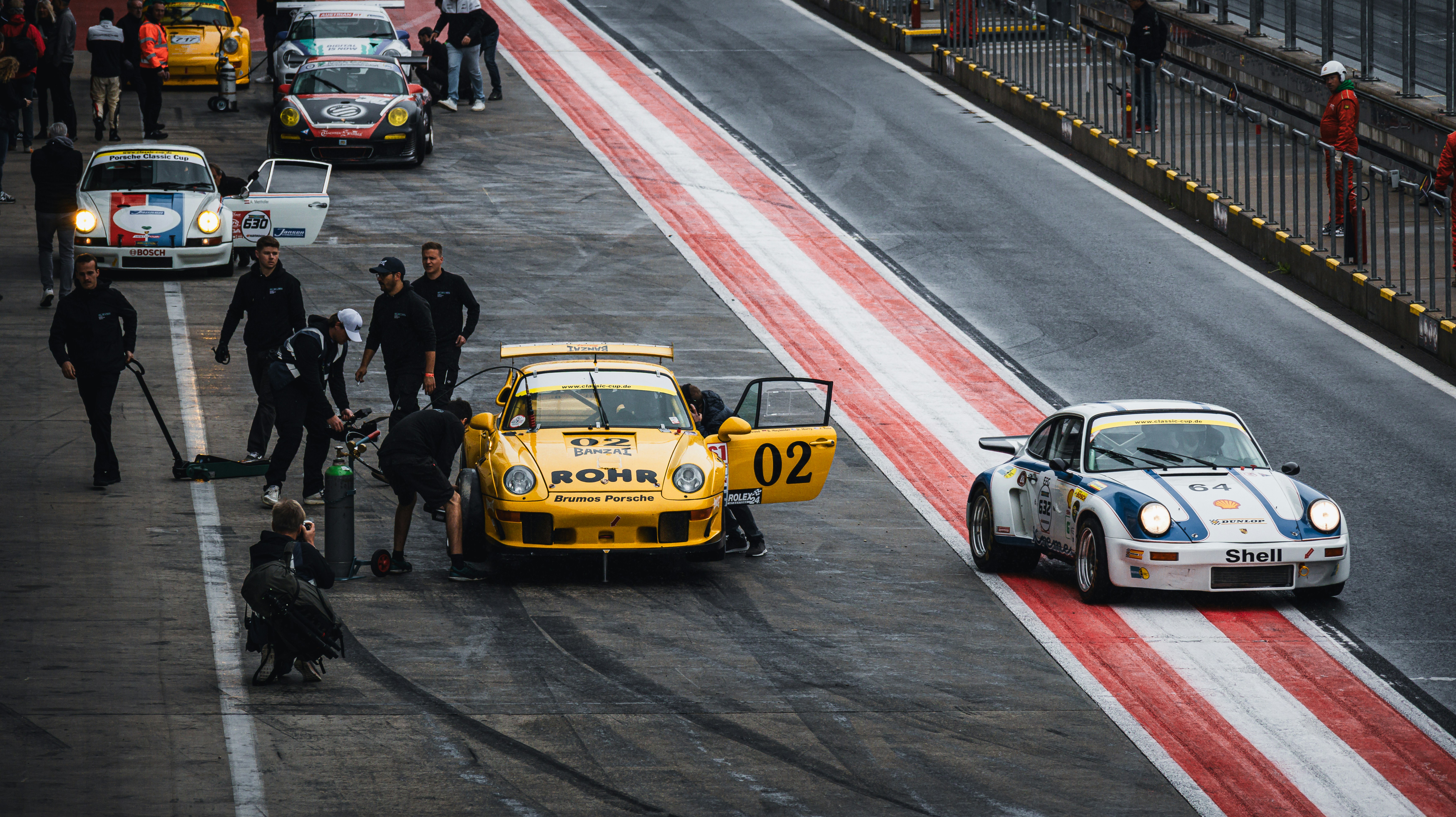 Race cars and their pit crews are preparing.