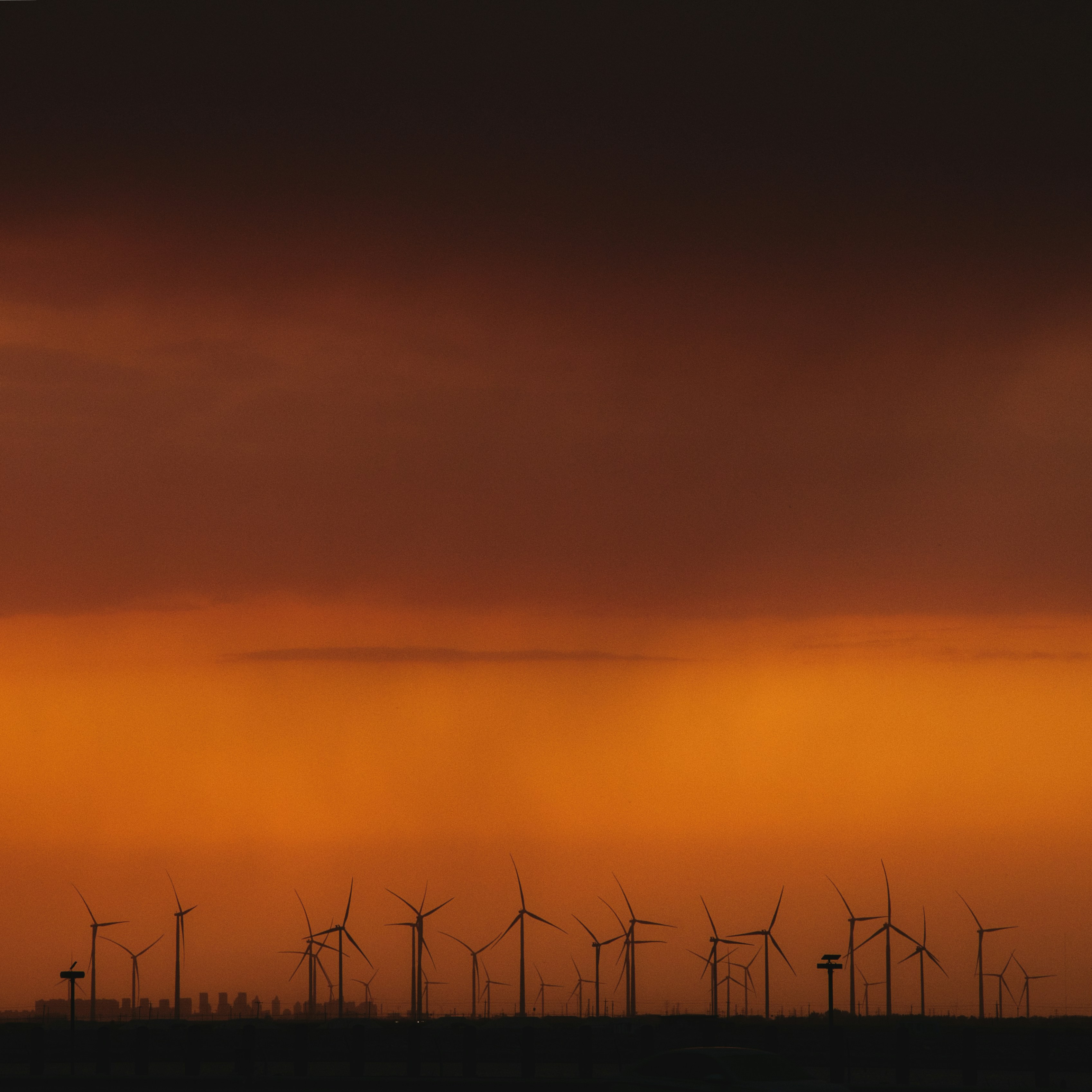 Wind turbines stand against a vibrant sunset.